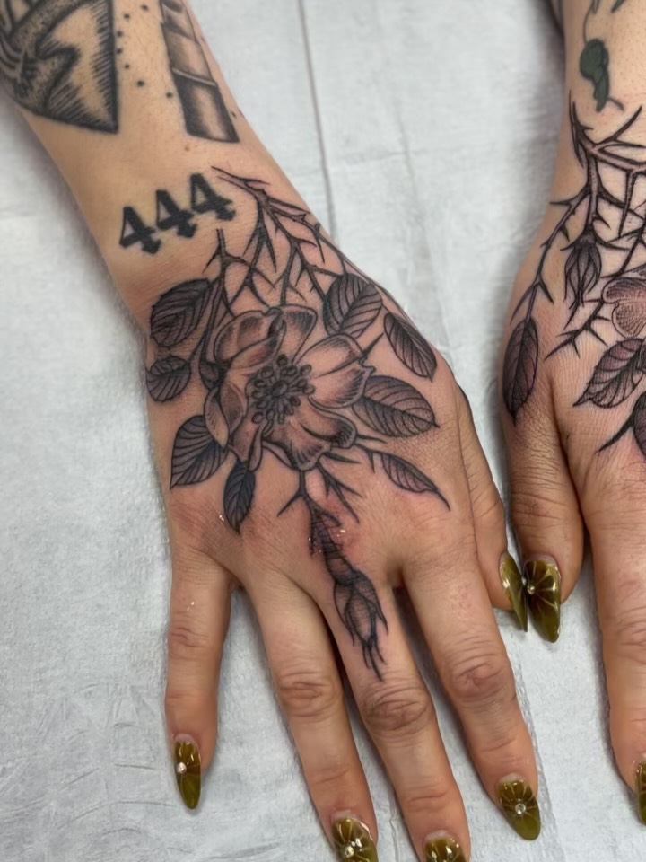 Bold black floral hand tattoo with delicate linework.