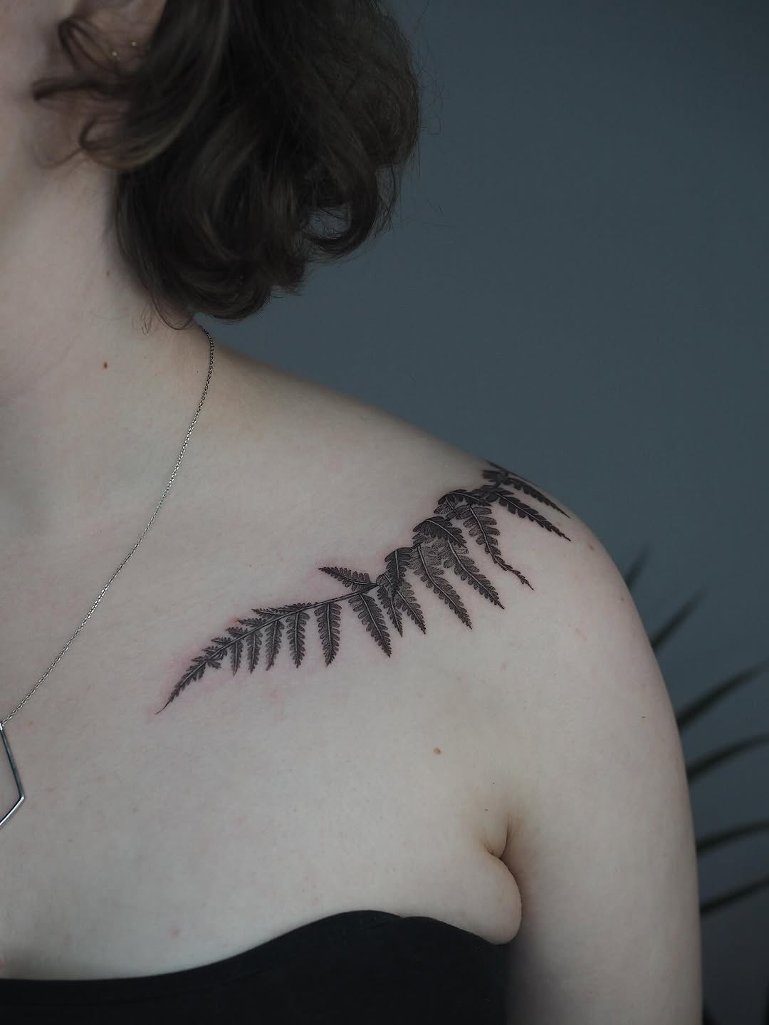 Elegant fern linework along the collarbone, delicate botanical.