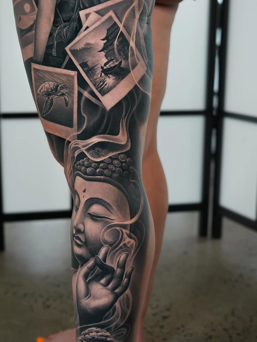 Monumental black-and-gray Buddha leg-sleeve with photoreal shading.