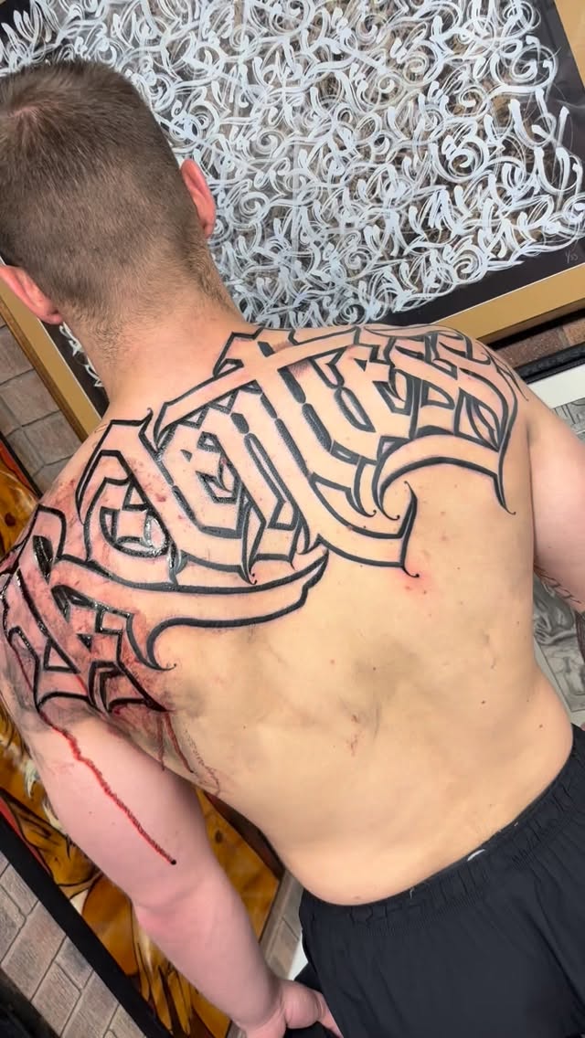 Bold black-line back piece with ornate geometric calligraphy.