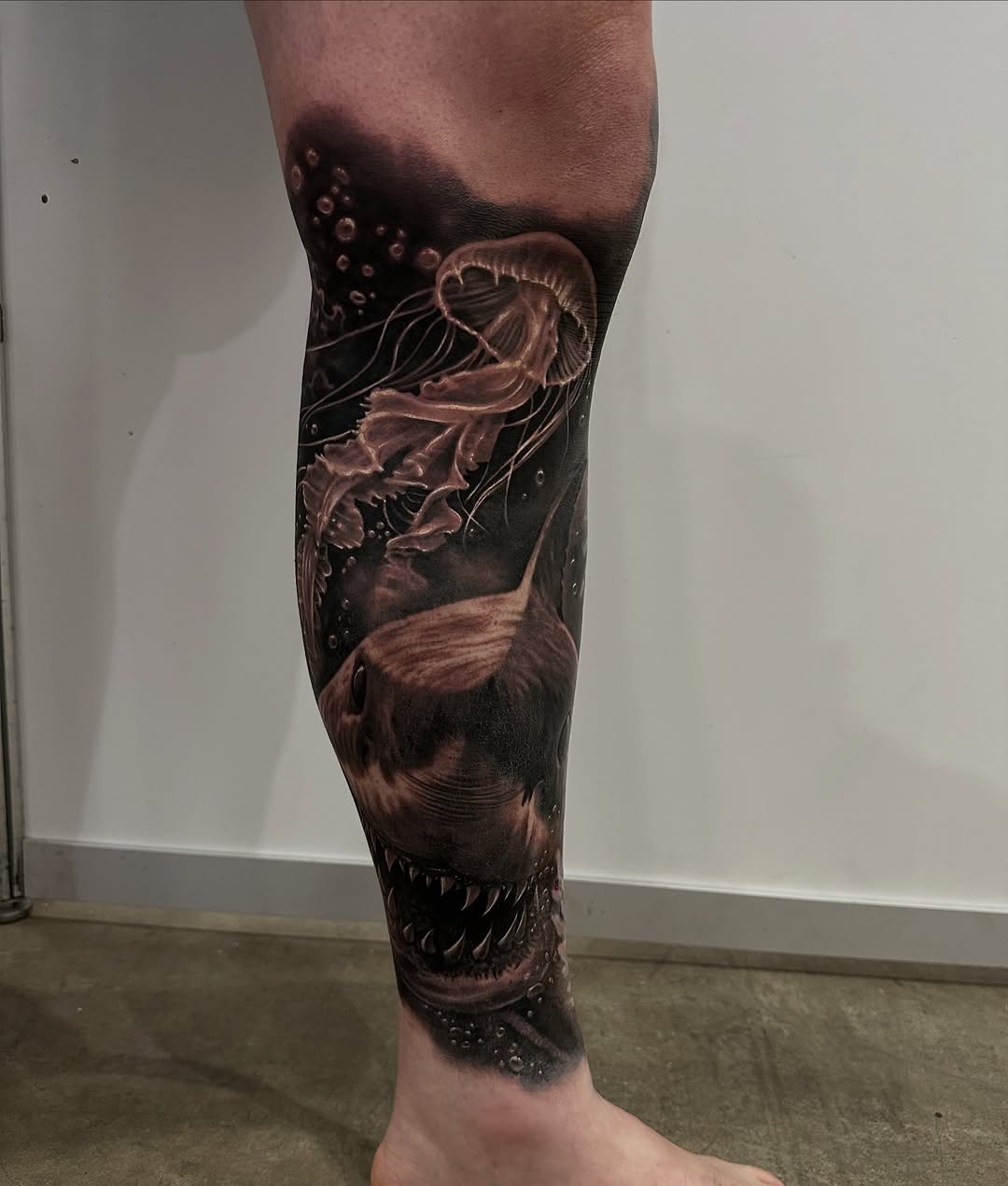 Hyperrealistic black-and-gray calf tattoo of shark and jellyfish