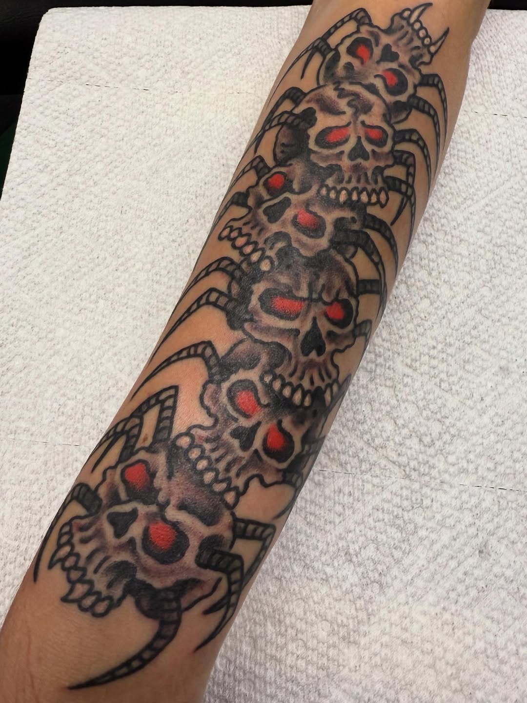 Chain of skulls with red eyes wraps forearm in blackwork