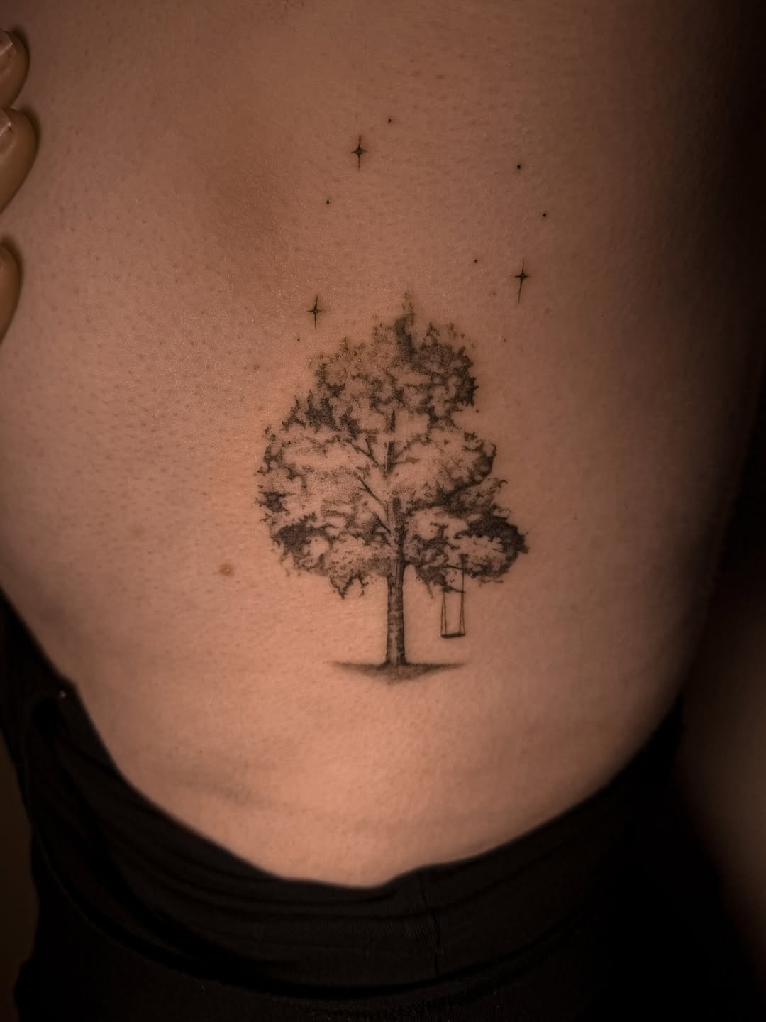 Delicate blackwork tree with a tiny swing and stars.