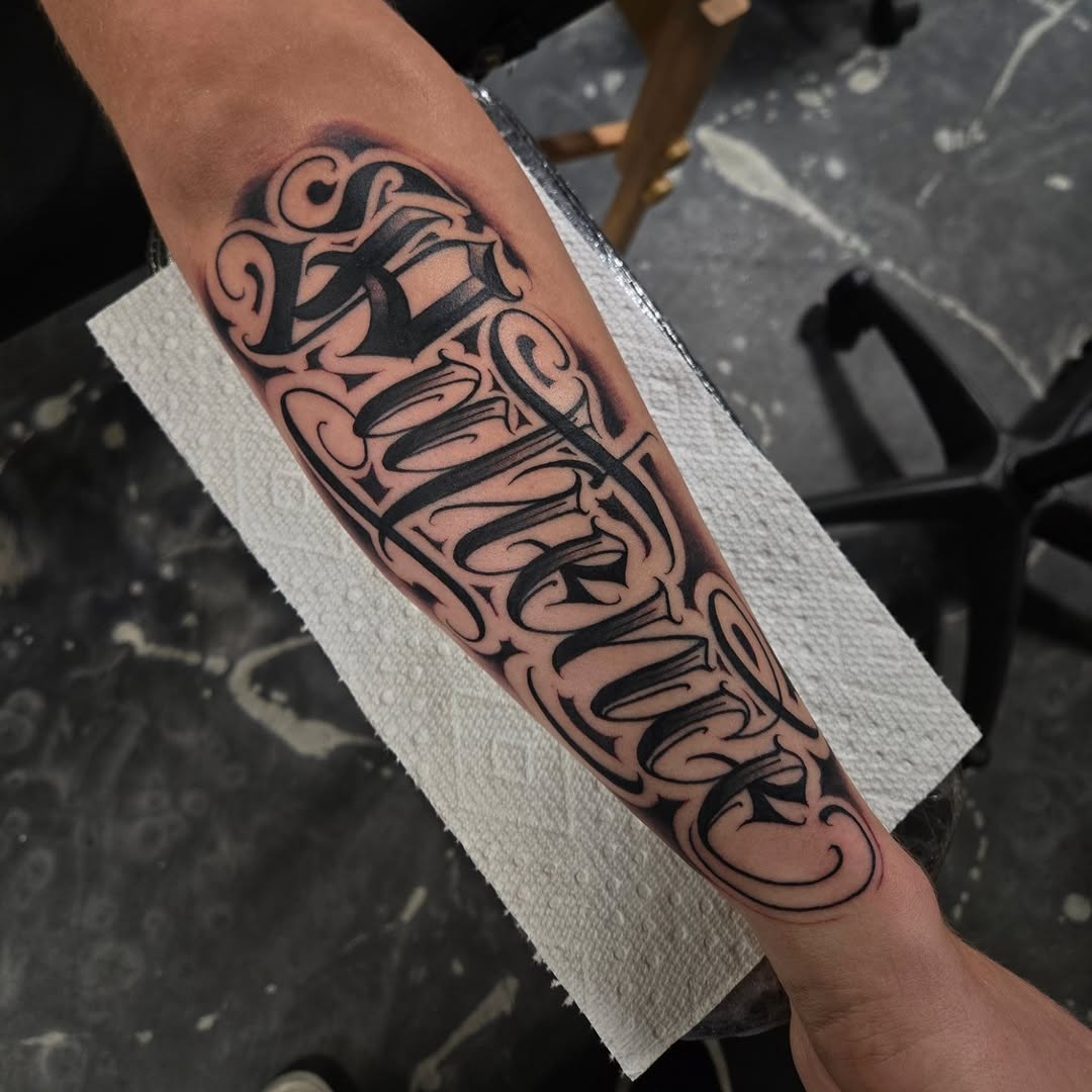 Bold blackletter script forearm tattoo with flowing flourishes
