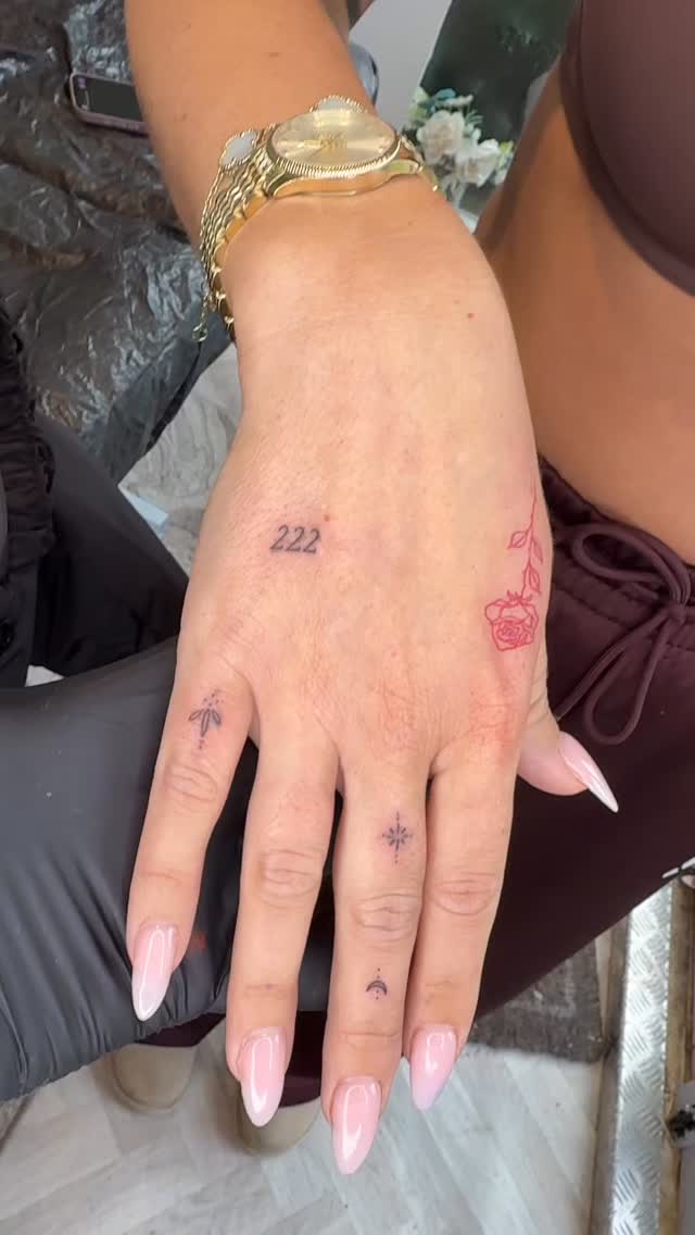 Delicate fine-line hand tattoos featuring tiny symbols and a rose.