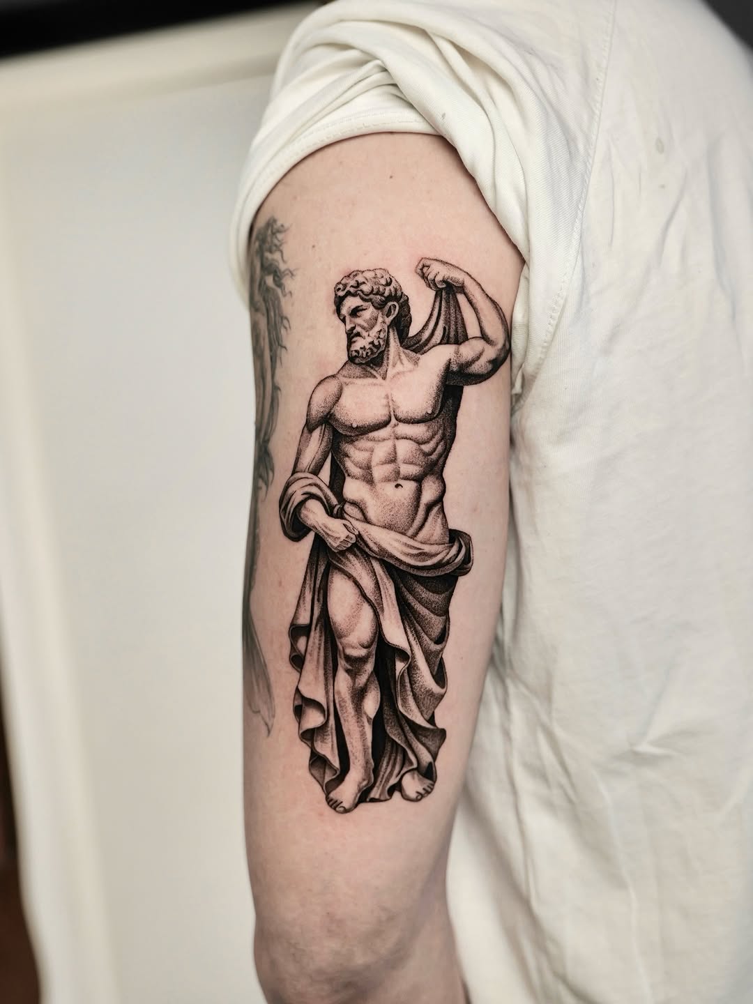 Neo-classical muscular statue with flowing drapery, black-gray shading.