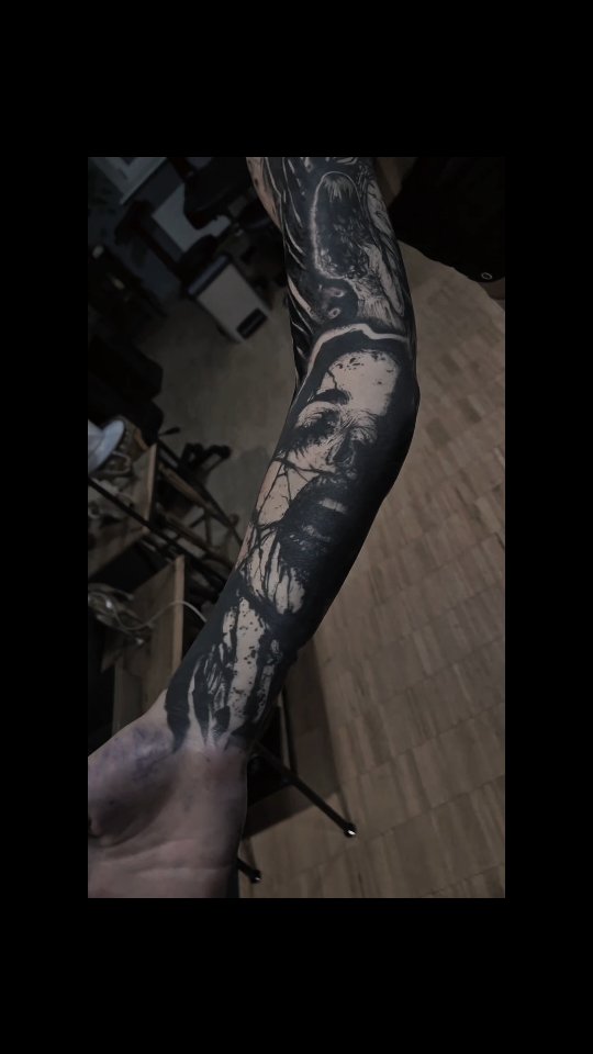 High-contrast blackwork forearm sleeve with skull-faced figures