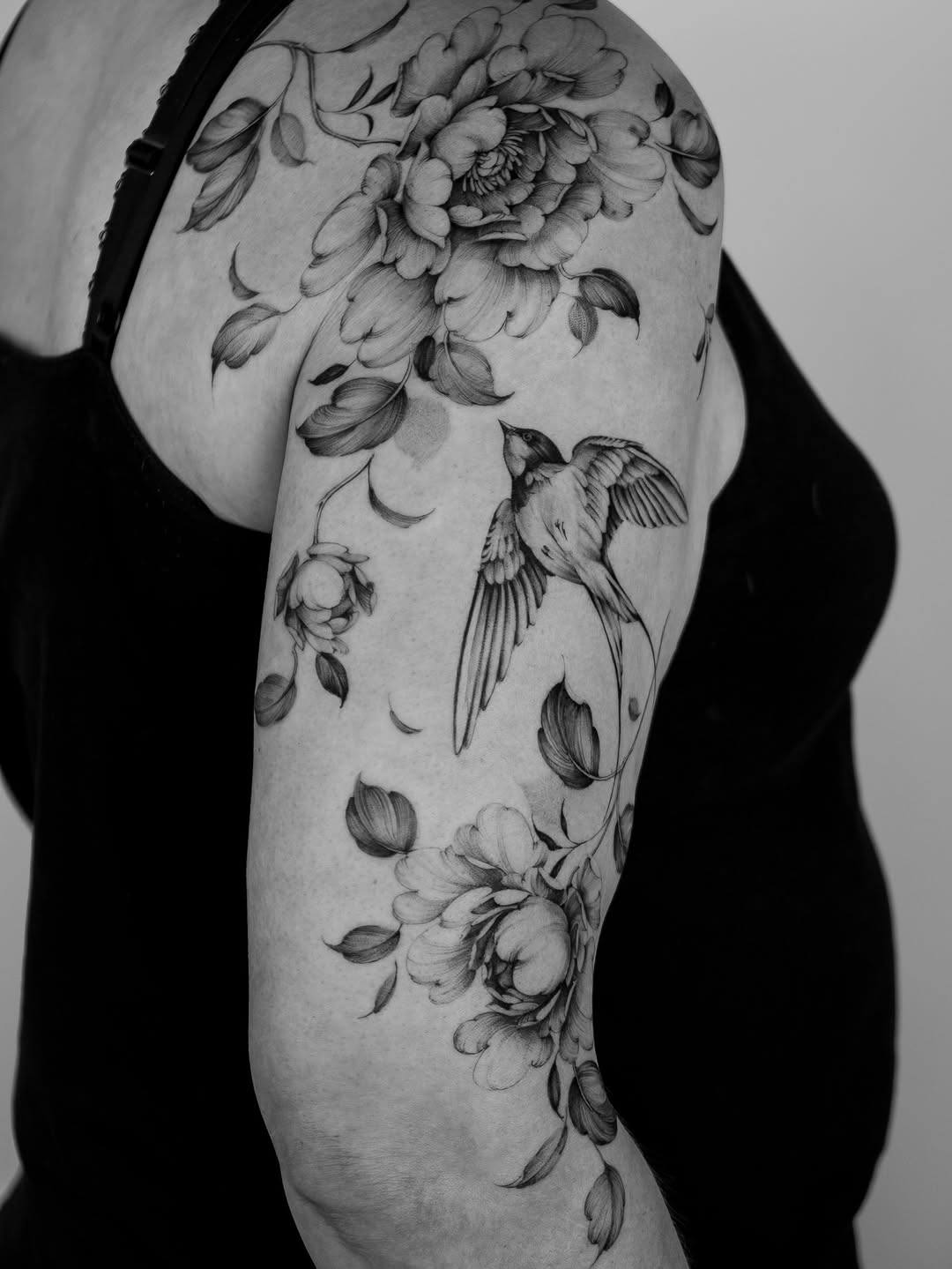 Delicate fine-line peonies and swallow on the upper arm