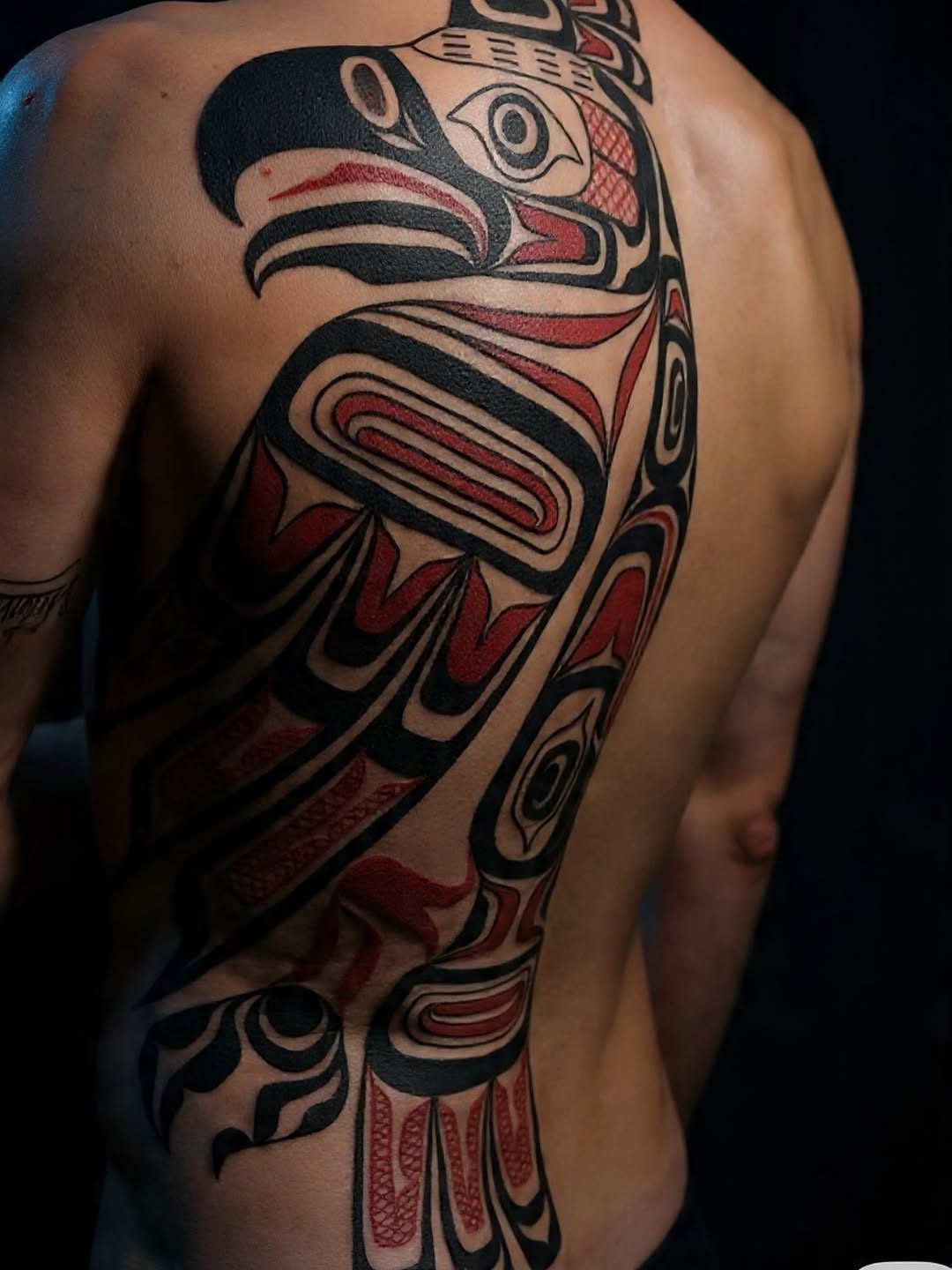 Bold northwest-coast tribal tattoo with black and red shapes