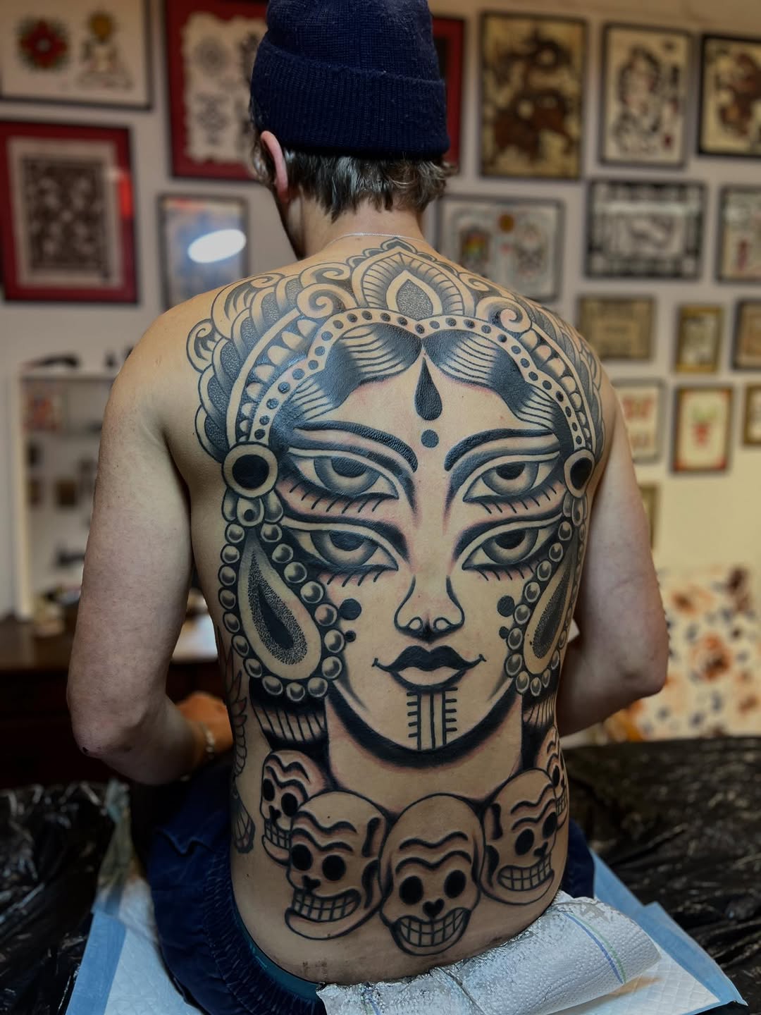 Intricate blackwork backpiece: deity-faced portrait with skulls.