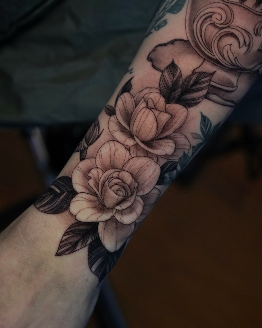 Intricate black-and-gray rose bouquet wraps forearm with shading.