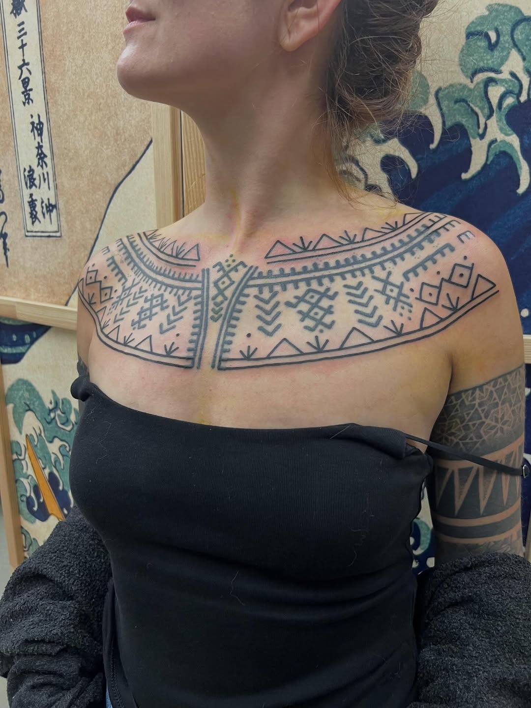 Bold black tribal-geometric chest piece across collarbone.