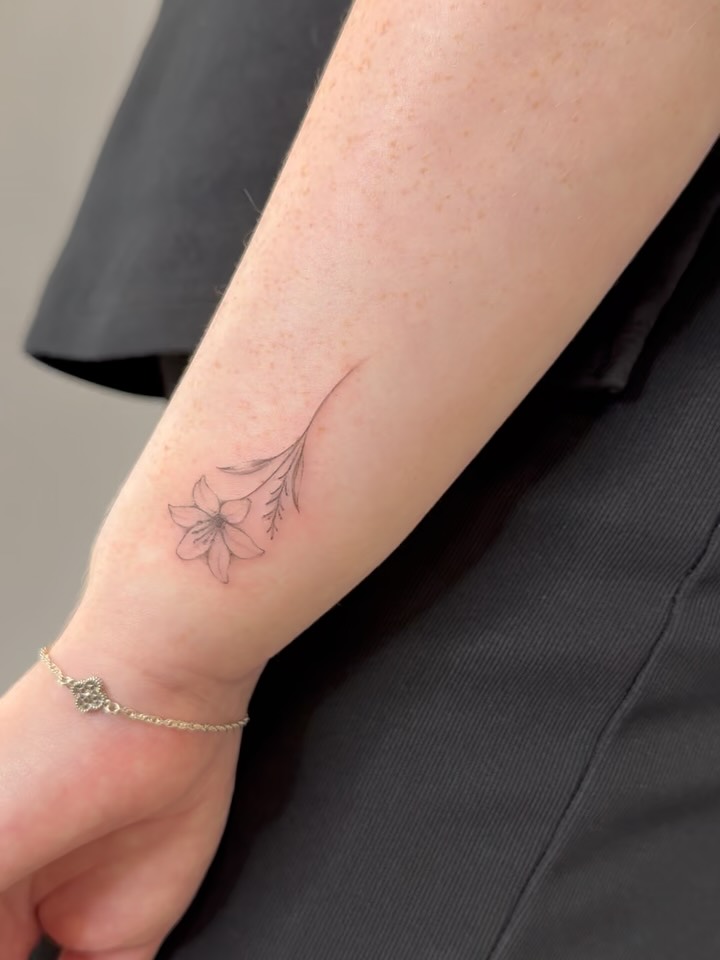 Delicate fine-line lily on inner forearm, soft greywash