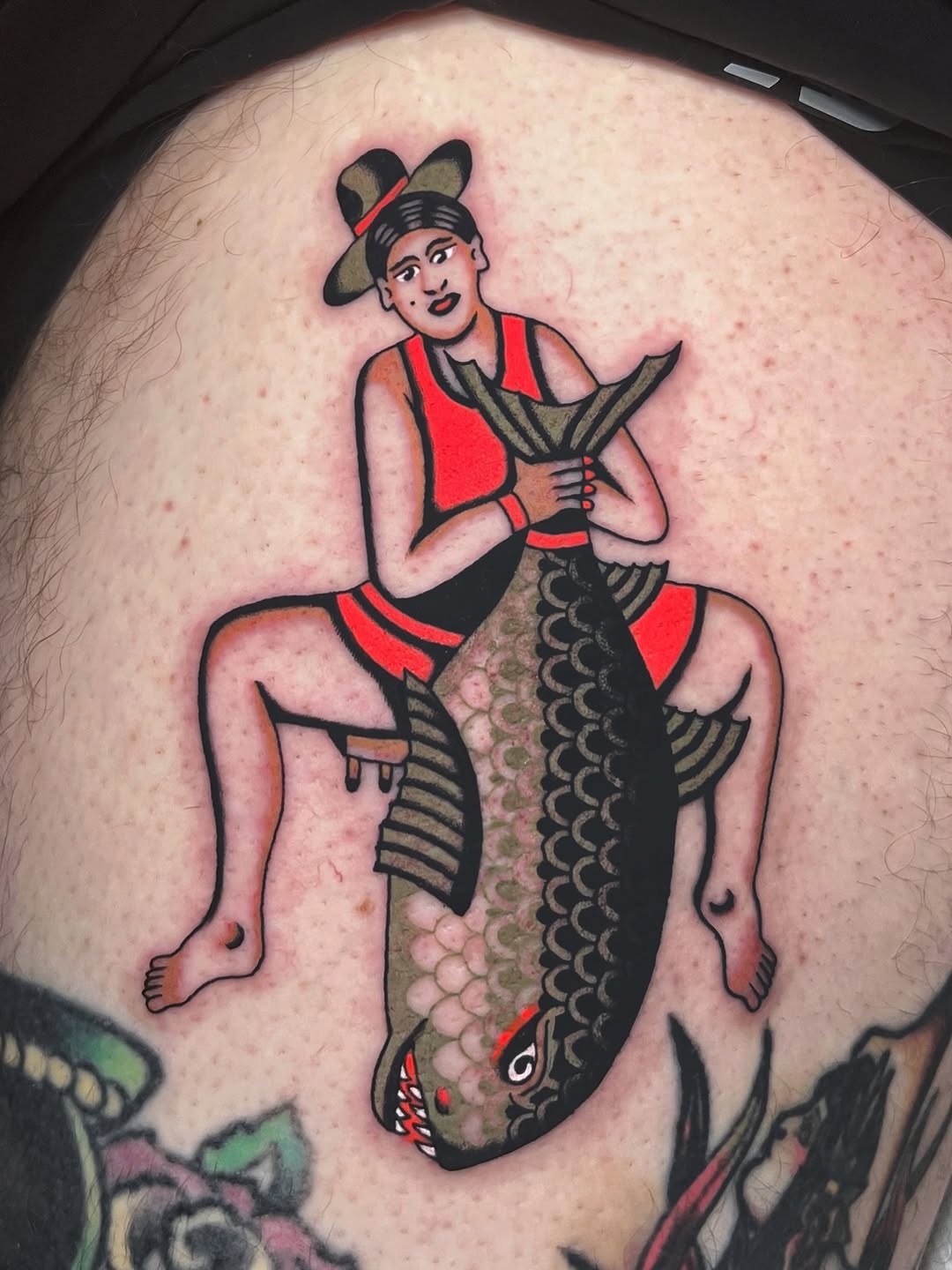 Bold traditional tattoo: woman perched on a giant carp, red dress.