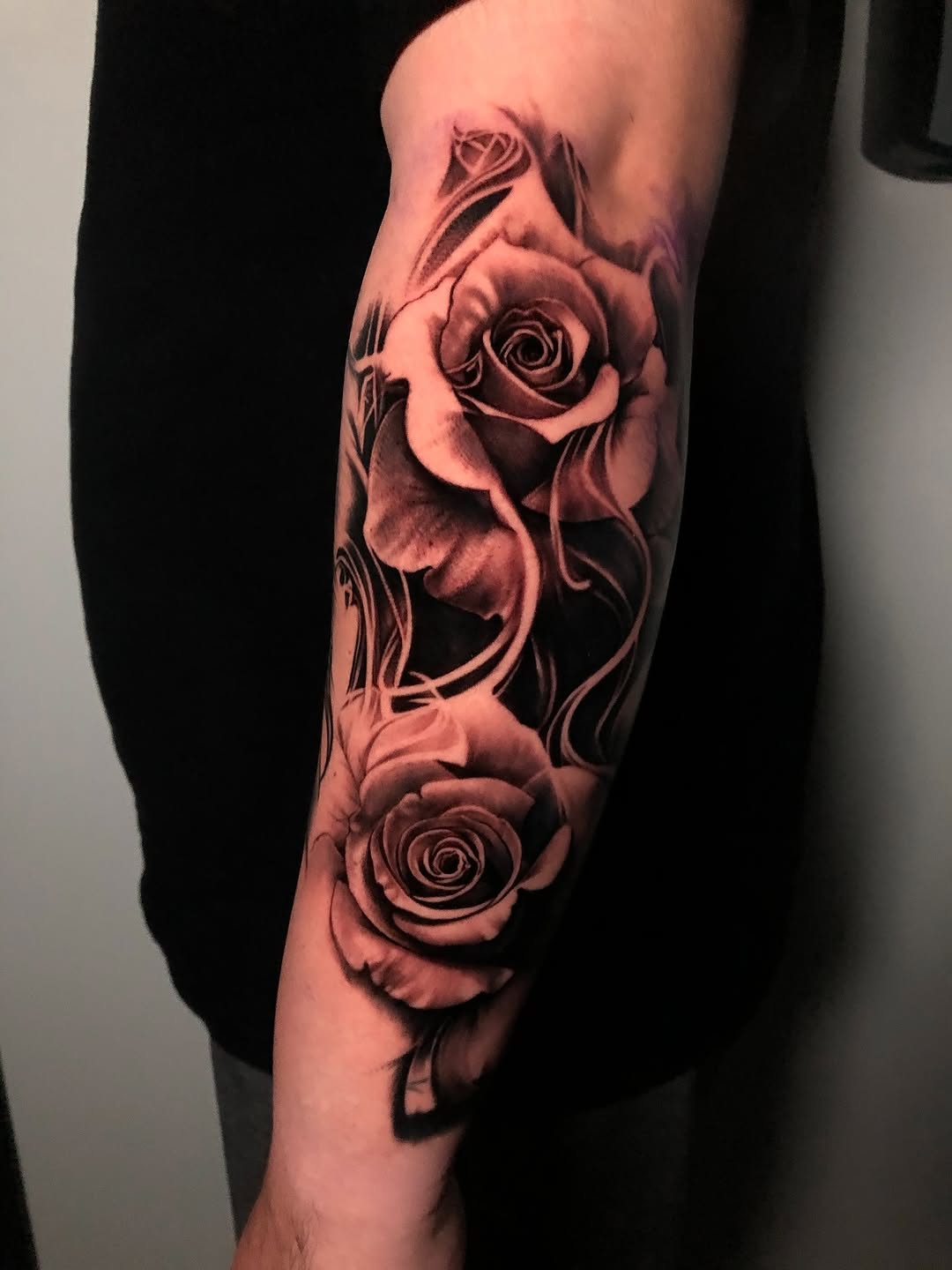 Hyper-realistic black-and-grey roses along the forearm.