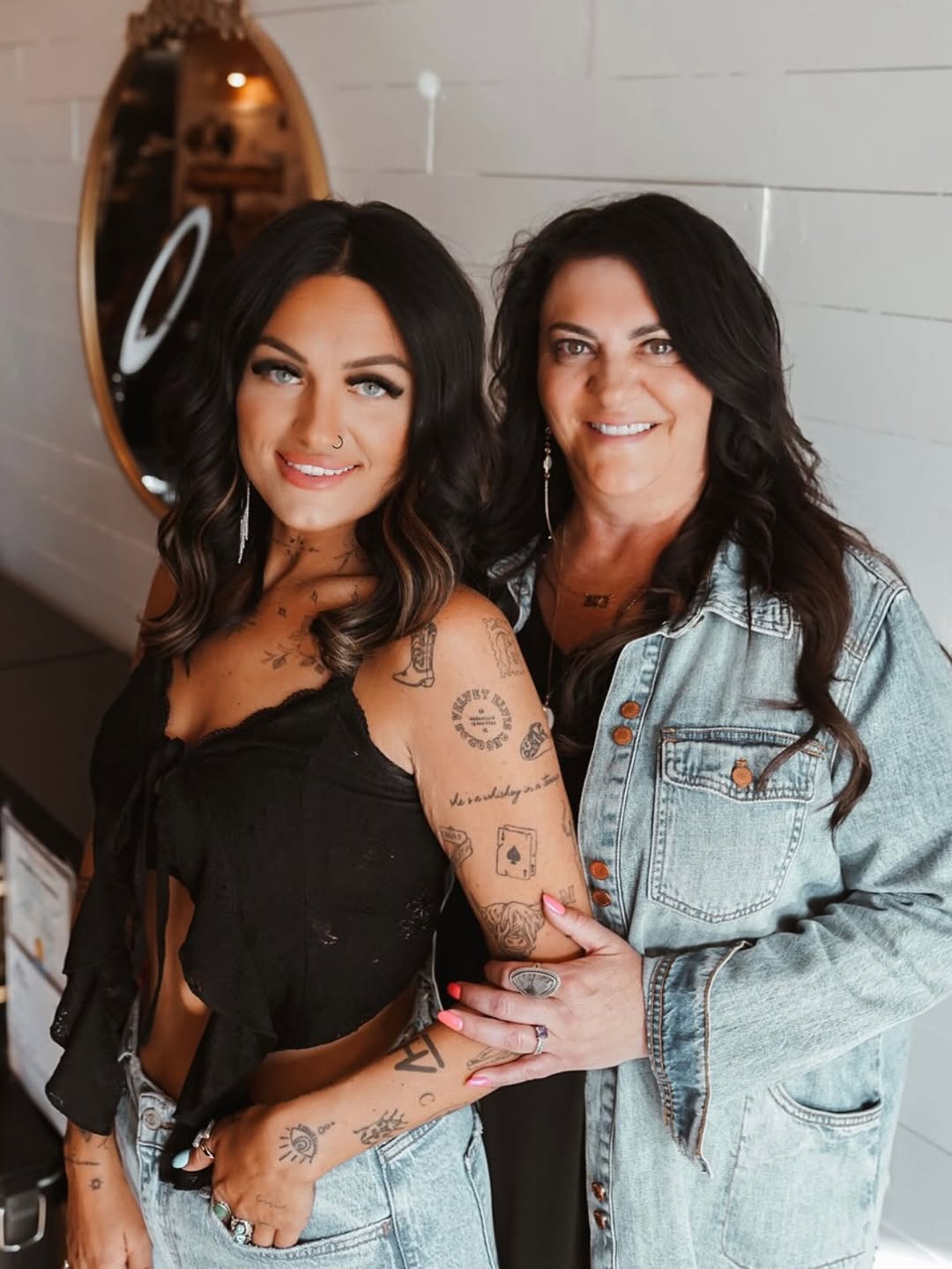 Bold black-line tattoos adorn forearm and shoulder, vibrant.