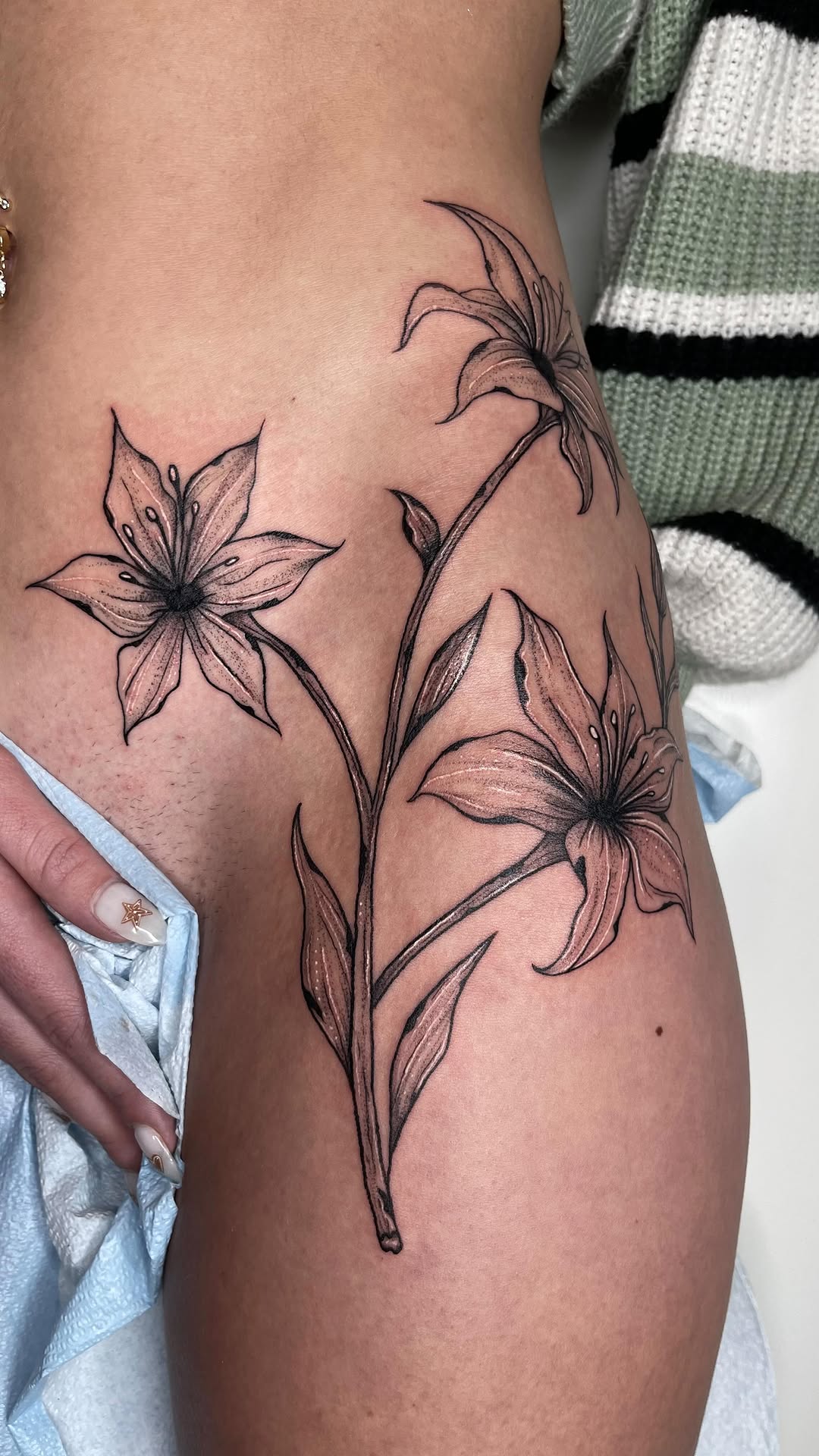 Elegant lily bouquet along the thigh, bold linework.