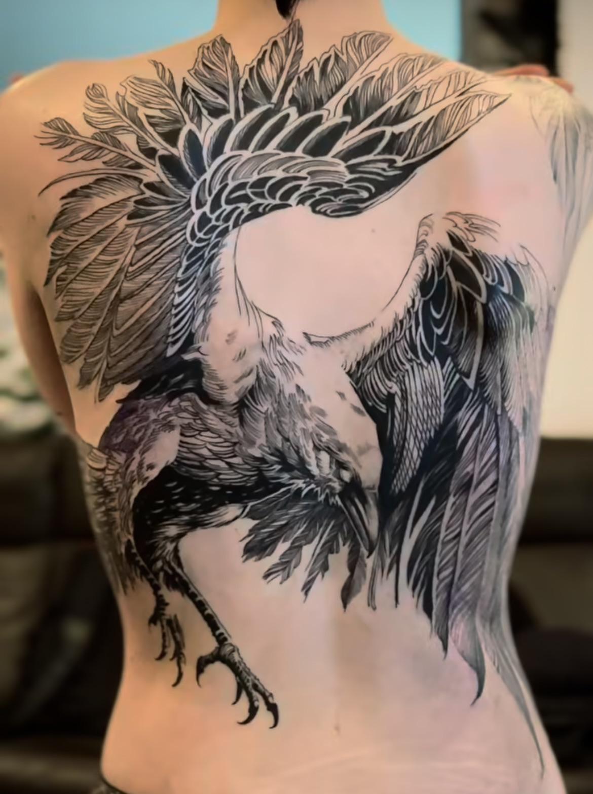 Massive blackwork raven with sweeping feathered wings across back