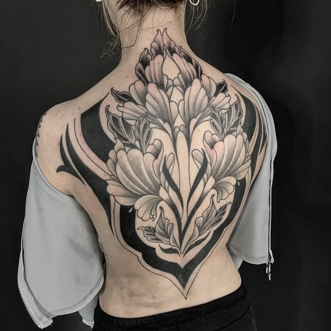 Art Nouveau-inspired blackwork floral back piece with bold shading.