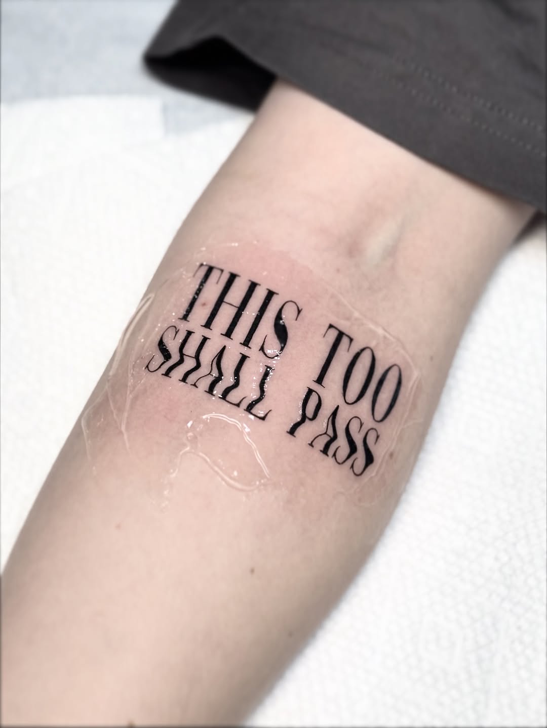 Elegant serif forearm quote: 'This Too Shall Pass'