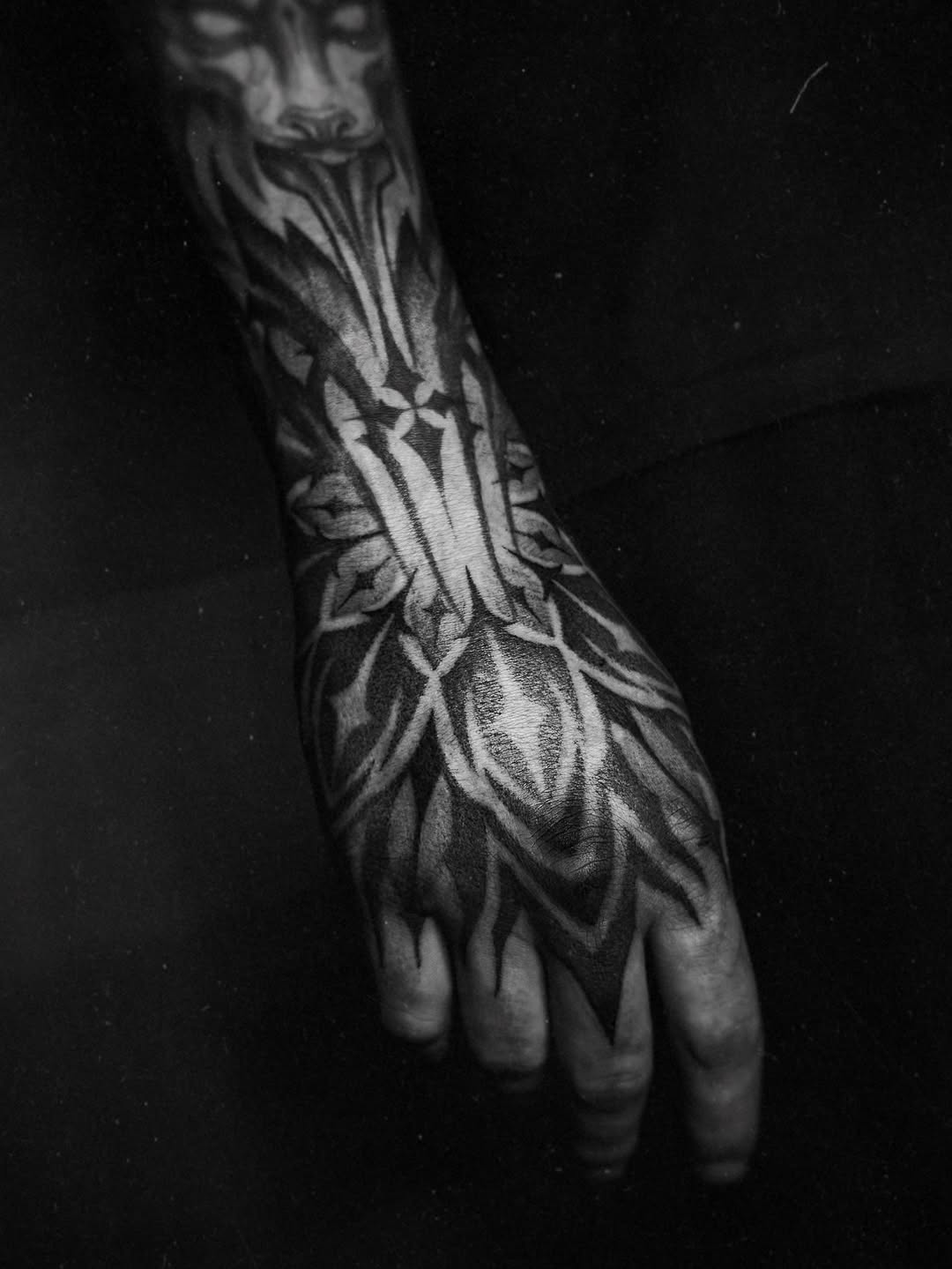 Intricate blackwork extension with geometric leaves across forearm.