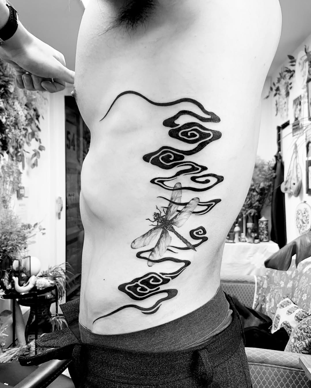 Bold blackwork rib piece with flowing cloud swirls and dragonfly