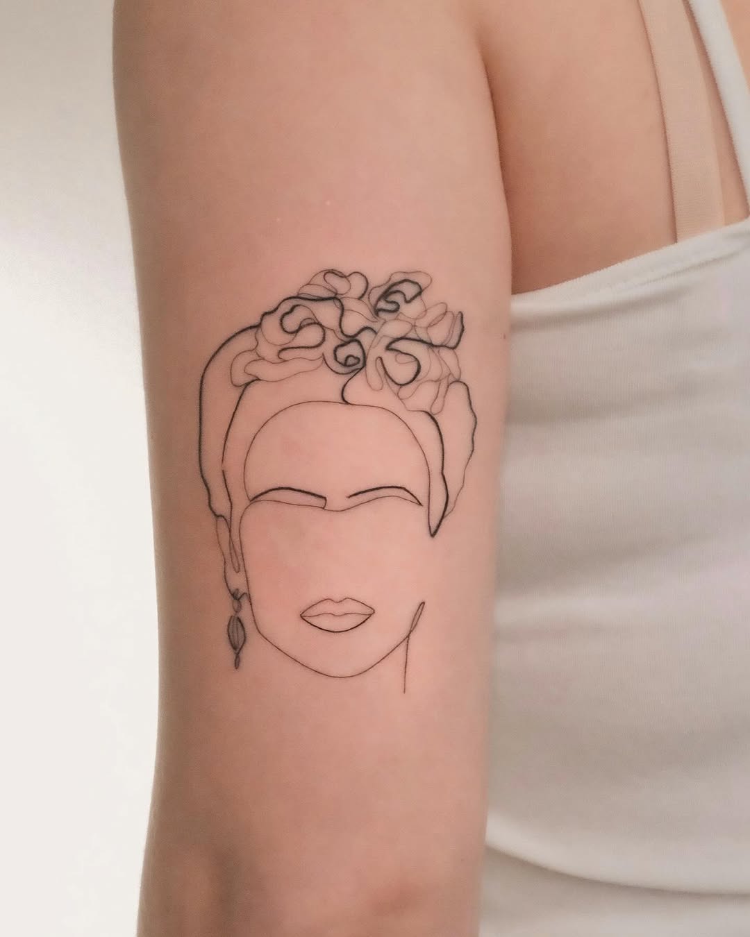 Frida Kahlo-inspired minimalist line portrait on forearm