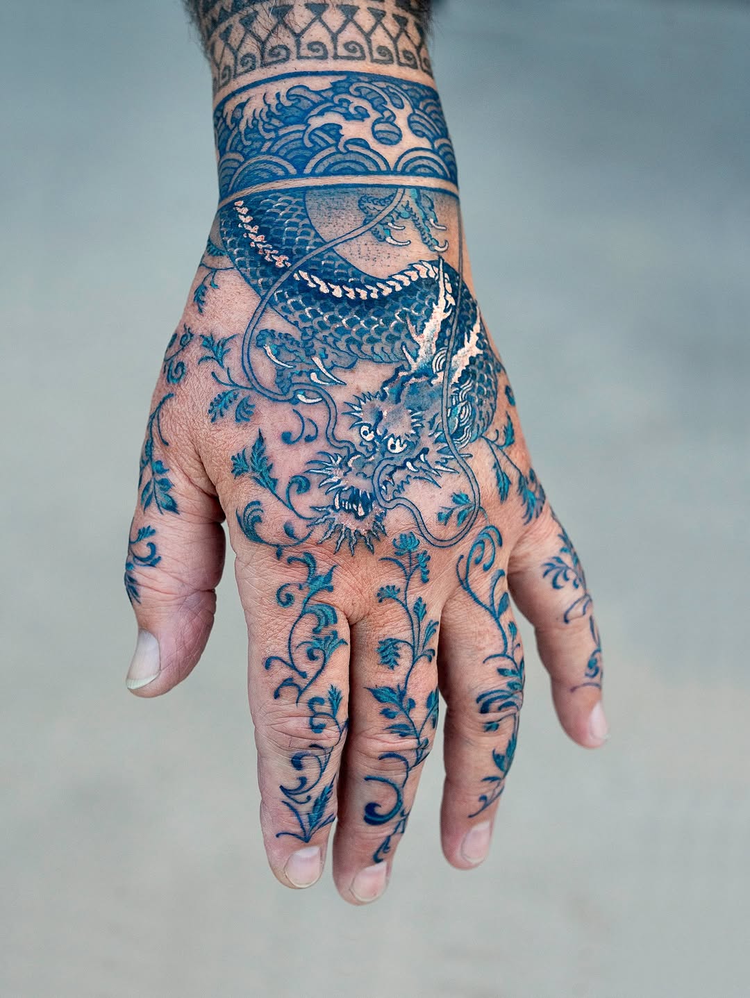 Intricate blue dragon entwined with floral vines across hand