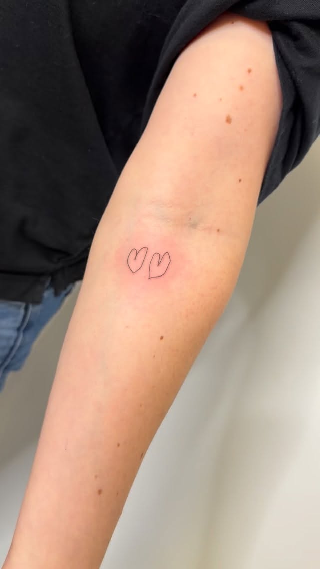 Delicate twin heart outlines in minimalist fine-line tattoo.
