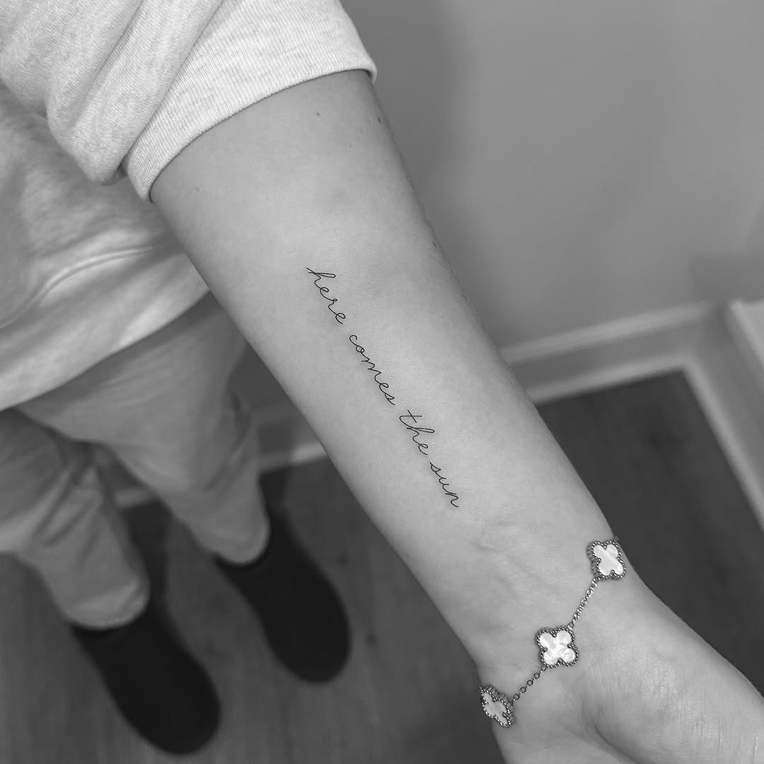 Elegant cursive 'here comes the sun' along inner forearm