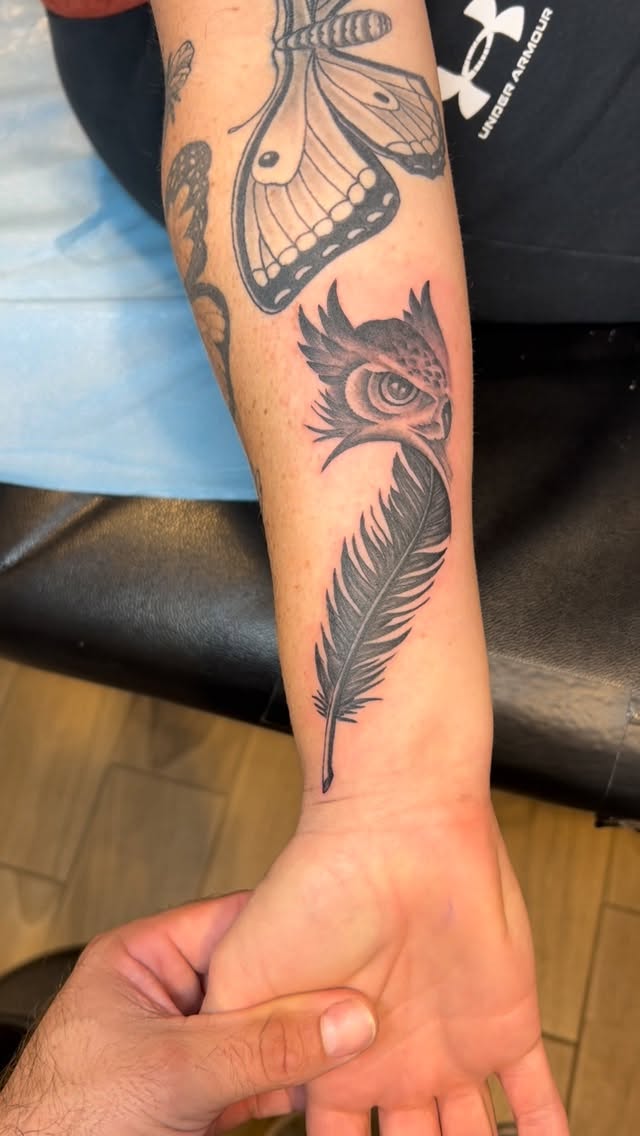 Monochrome feather flows along forearm with bold butterfly.