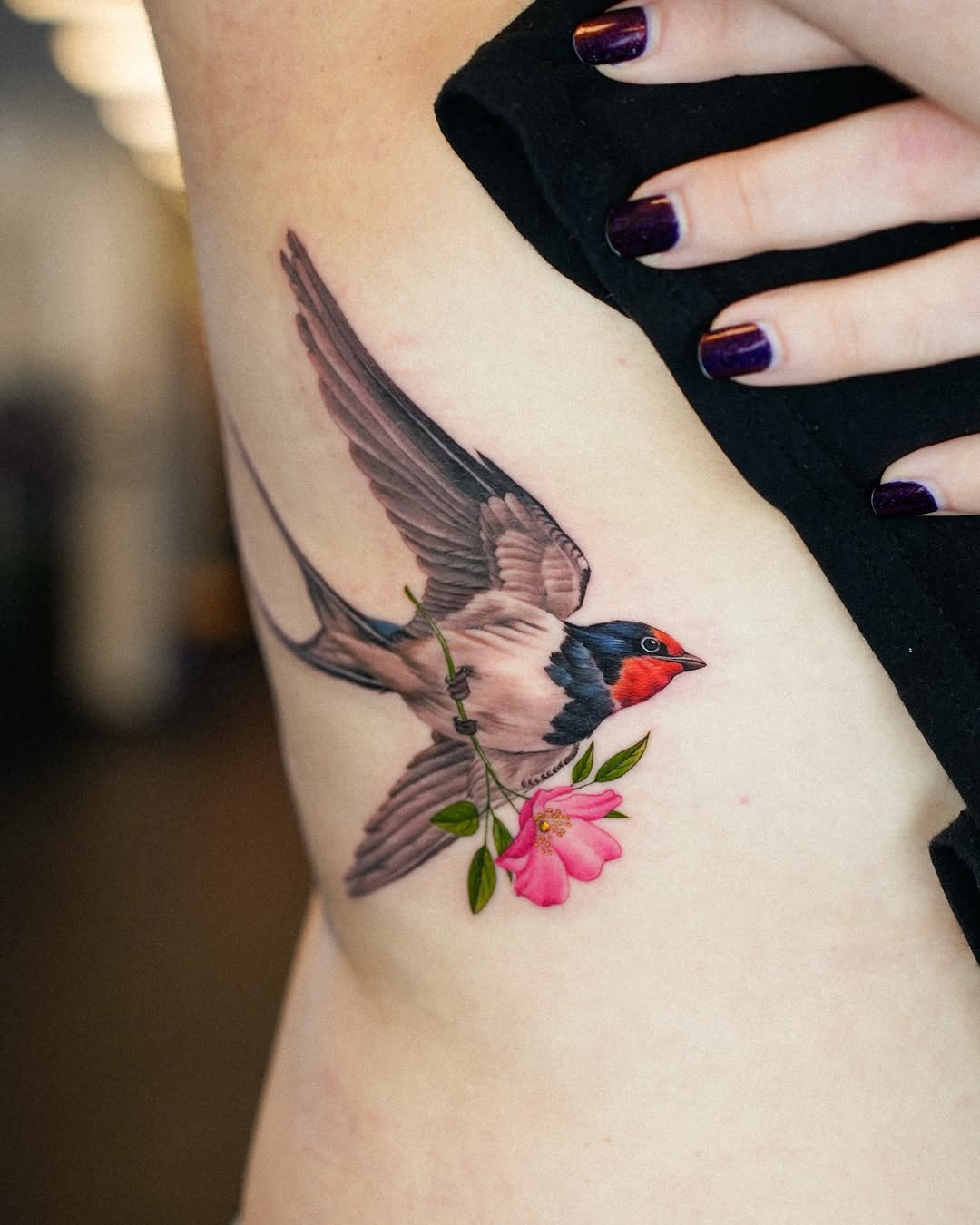 Vivid swallow in flight clutching a pink flowering stem