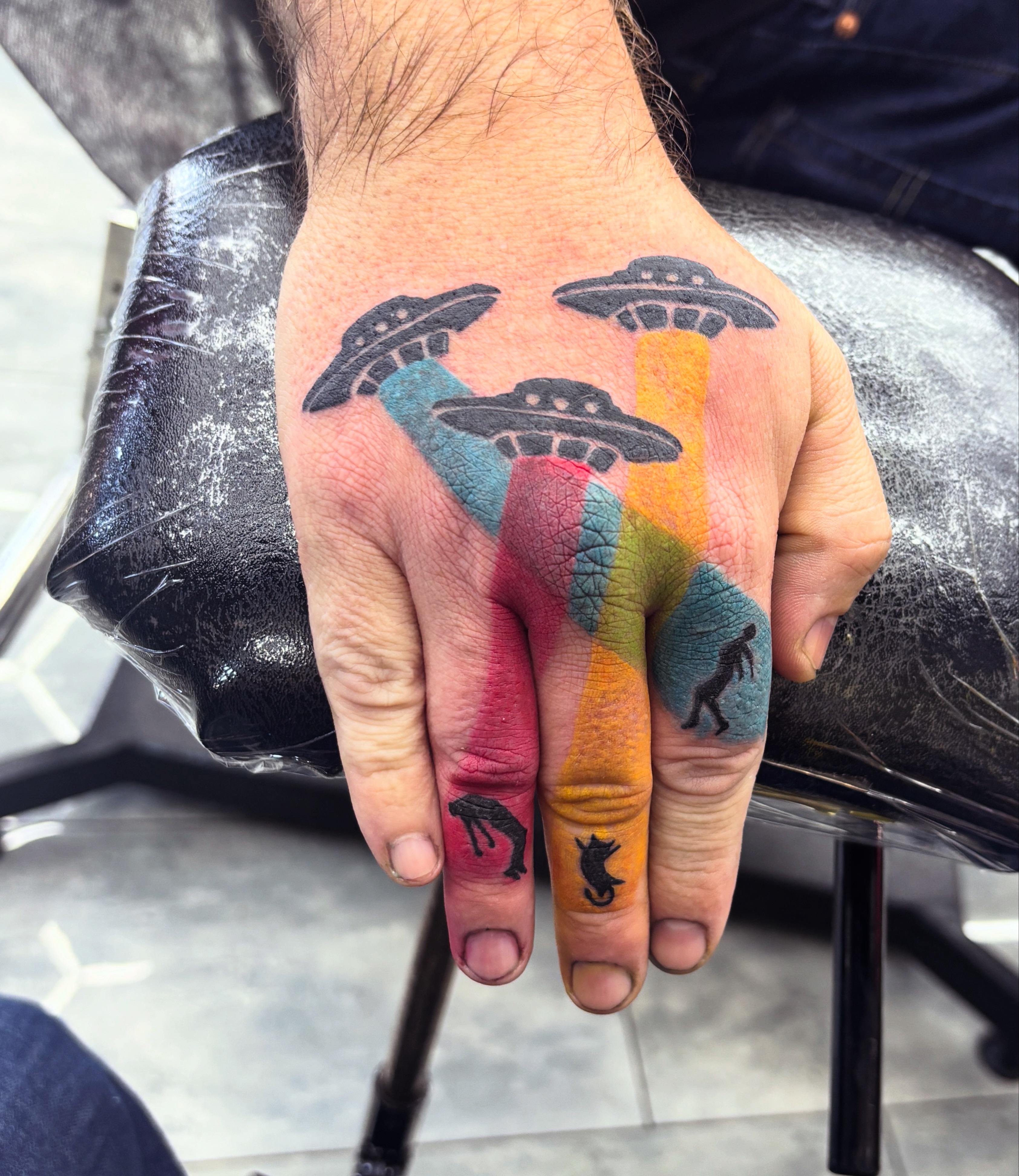 Vibrant hand tattoo with flying saucers and color blocks