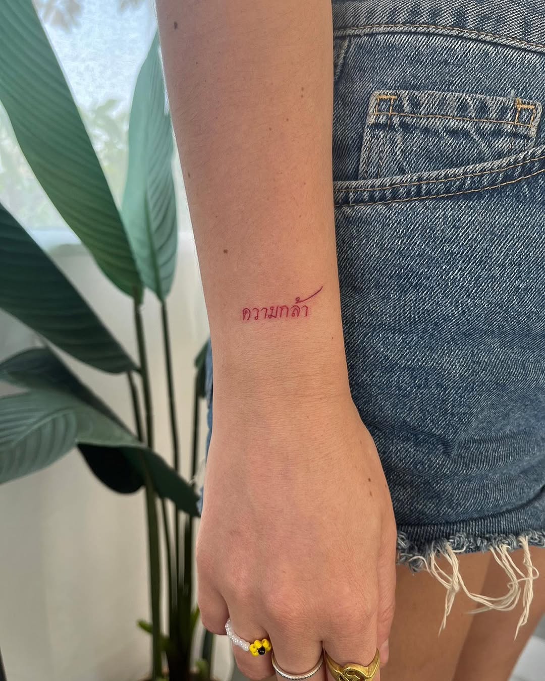 Slim red Thai script 'ความกล้า' on inner forearm.