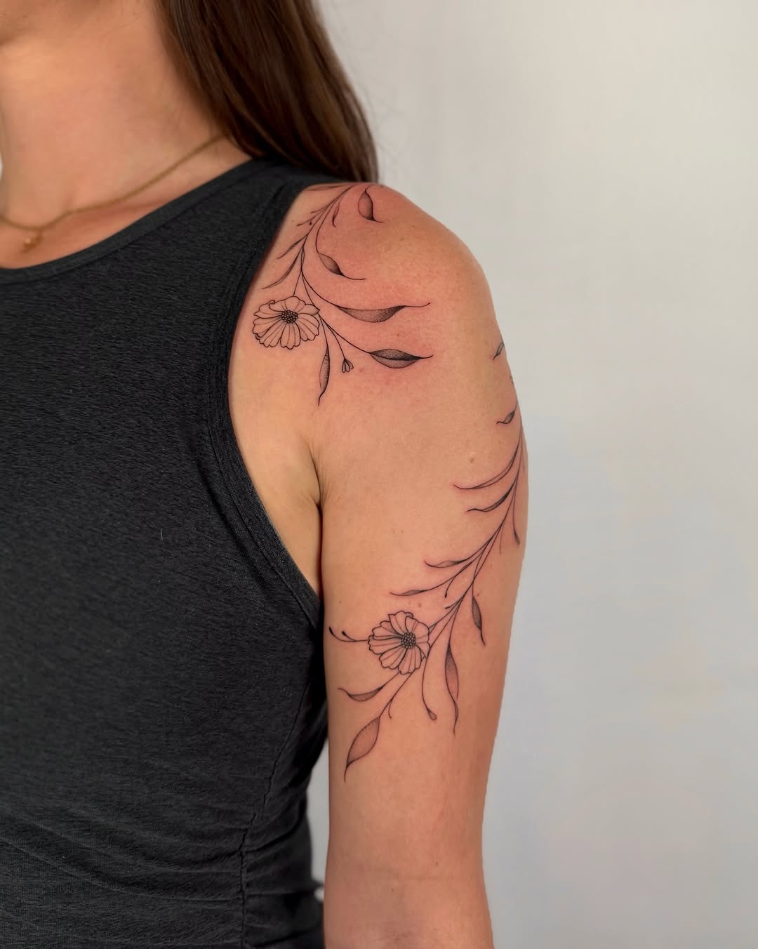 Delicate fine-line floral vine wraps shoulder with daisies.