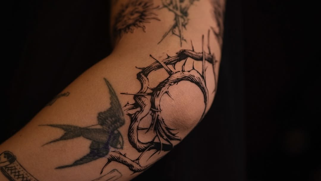Bold linework swallow encircled by thorn crown on forearm.
