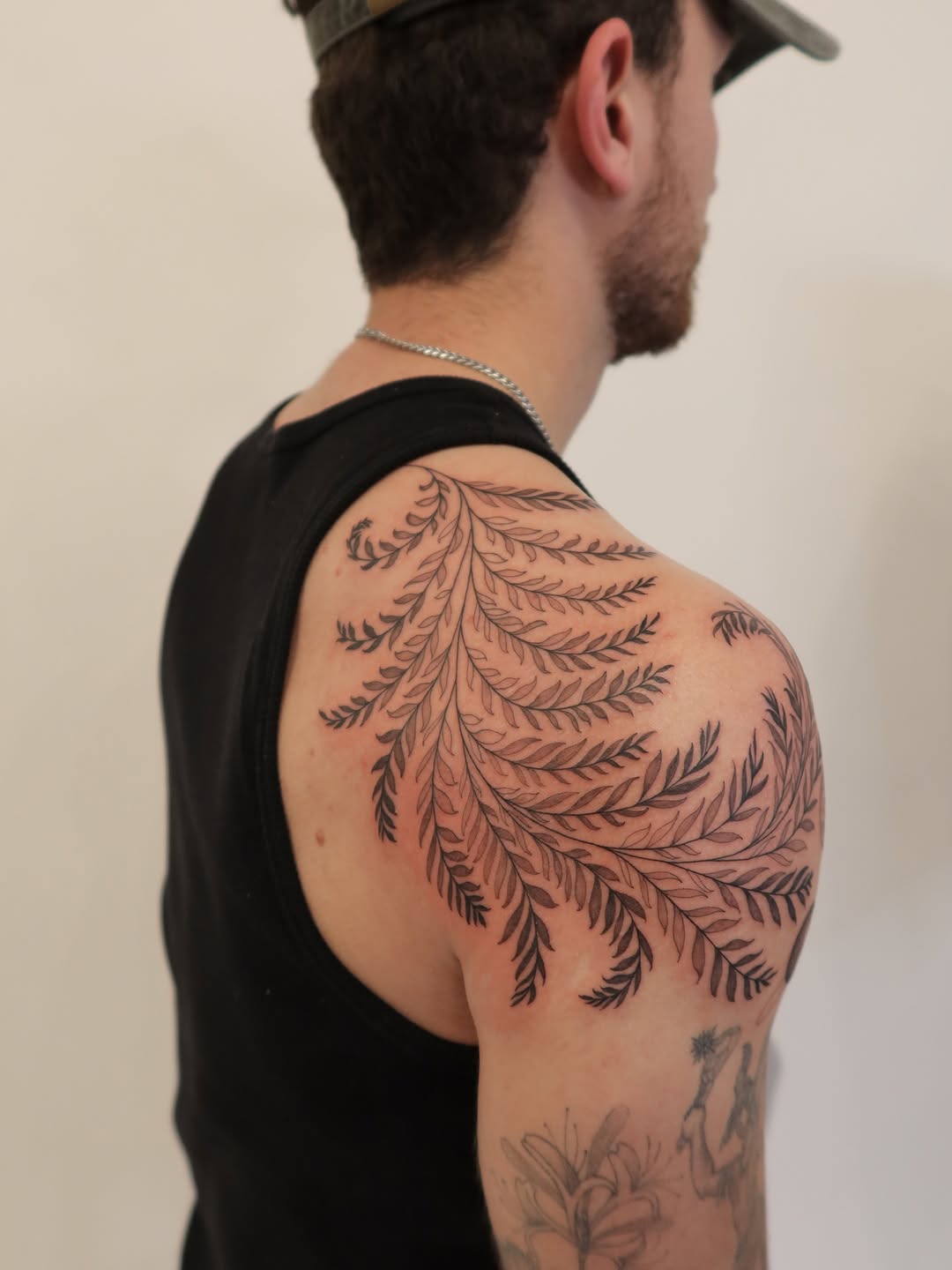 Bold black fern fronds wrap shoulder in crisp linework.