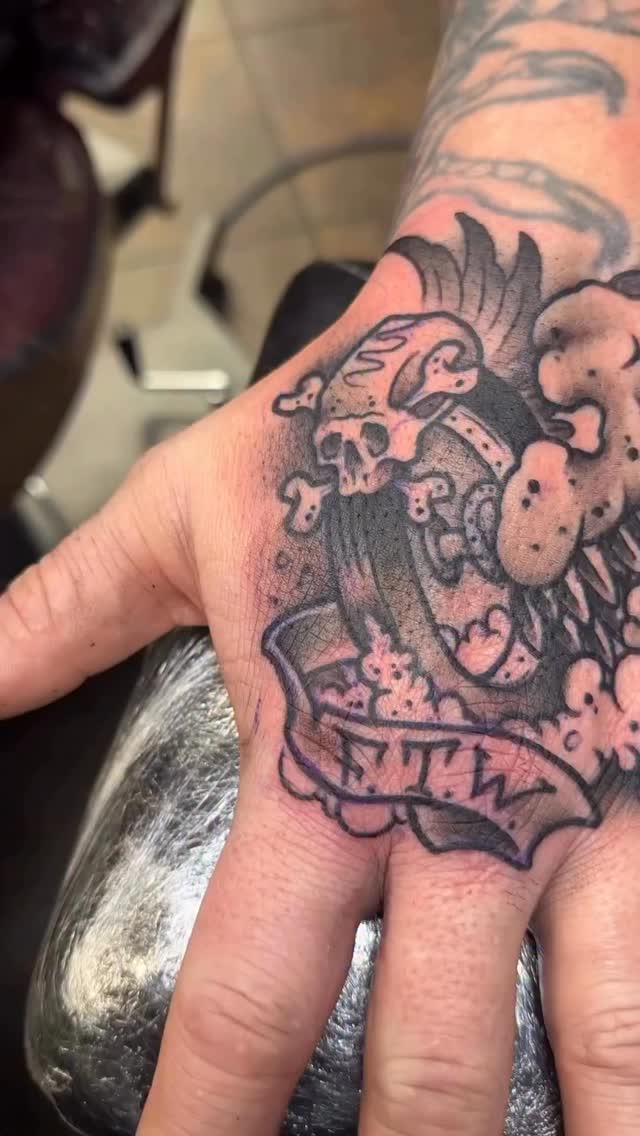 Bold traditional hand tattoo with banner and skull motifs