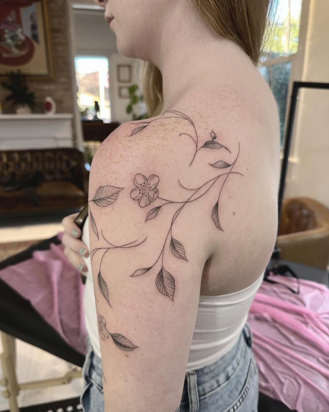 Delicate fine-line floral vine wraps shoulder with leaves.