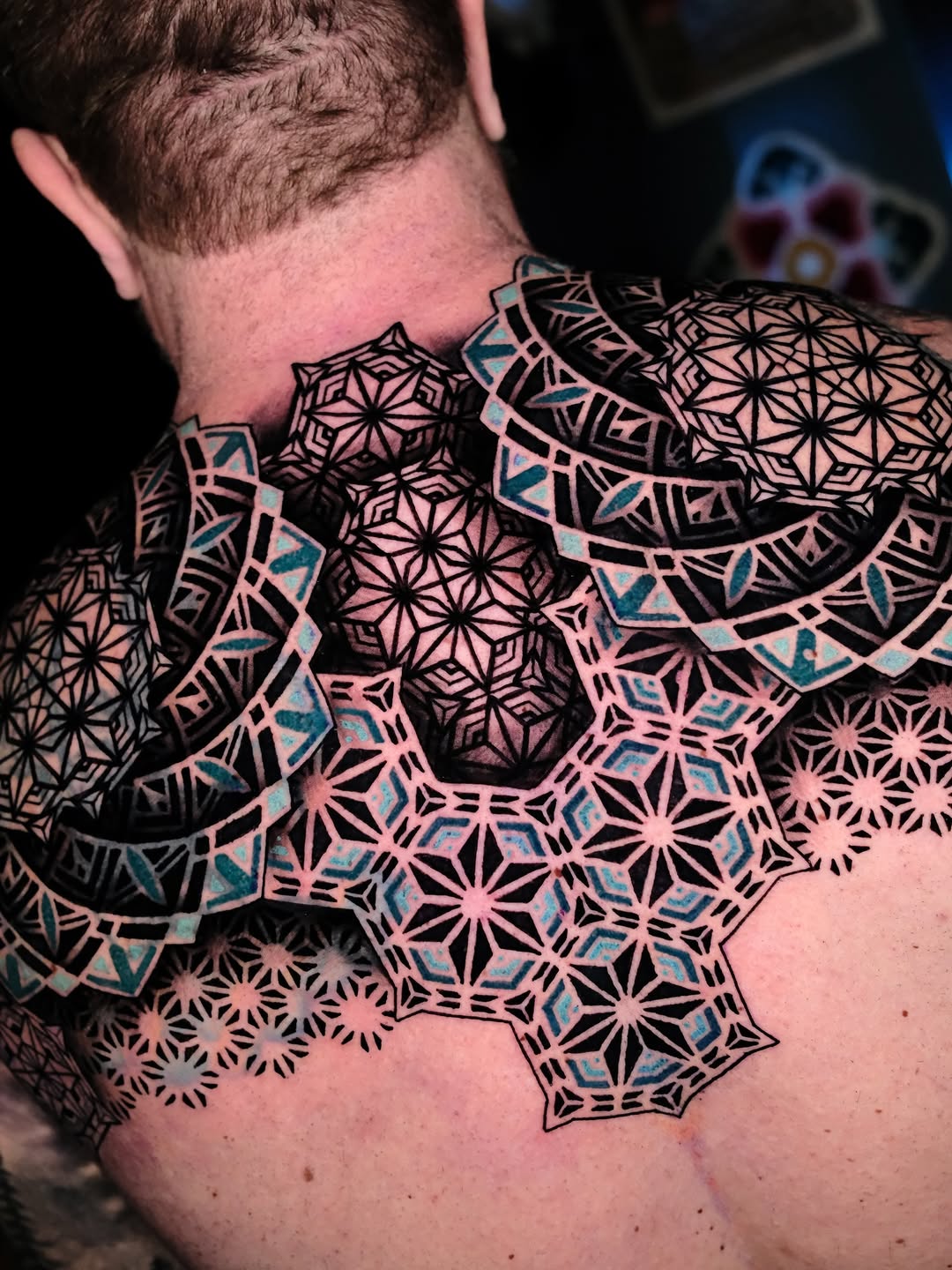 Bold geometric mandalas cover neck and shoulder, teal accents.
