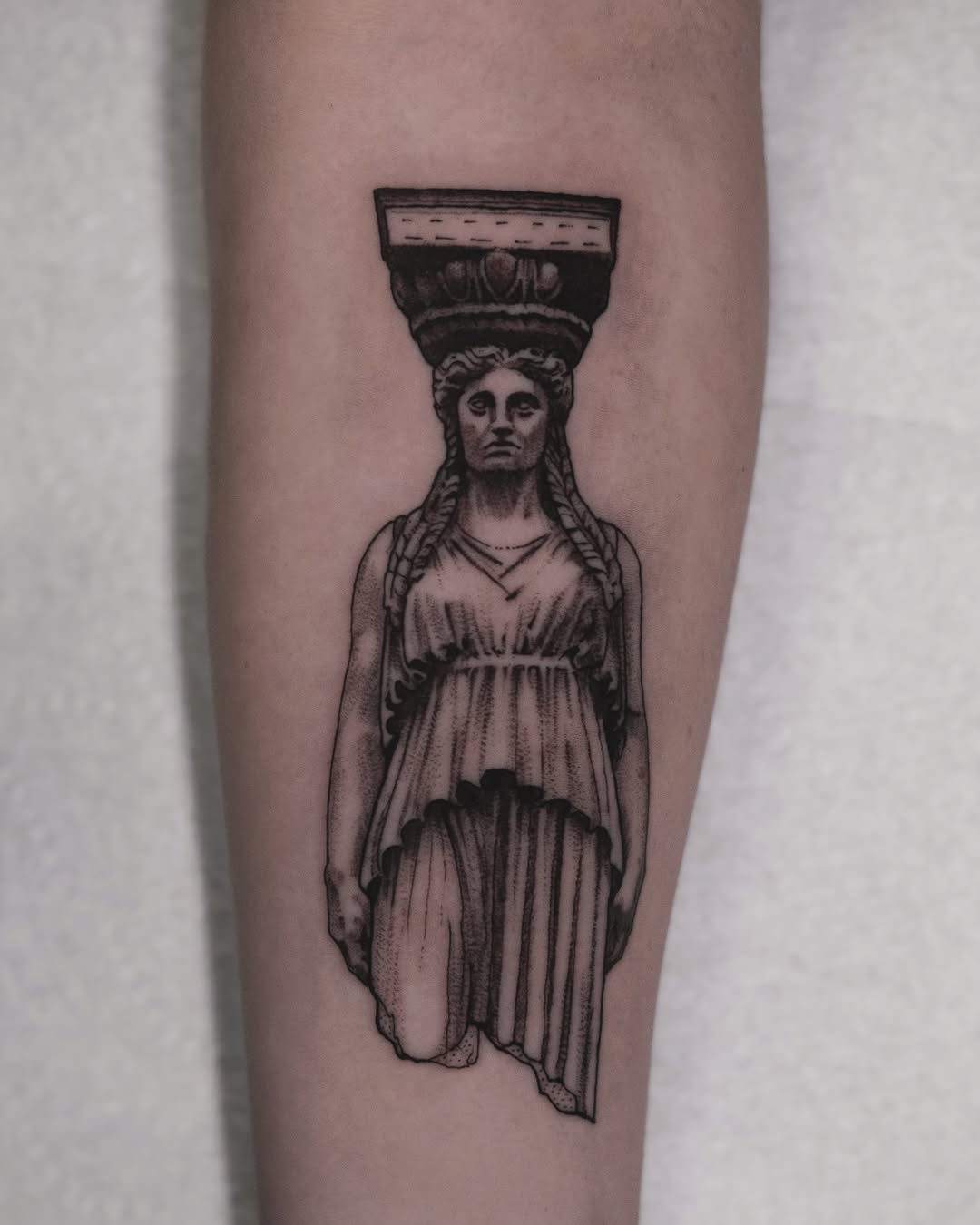 Statue-like female in flowing robe beneath a column capital