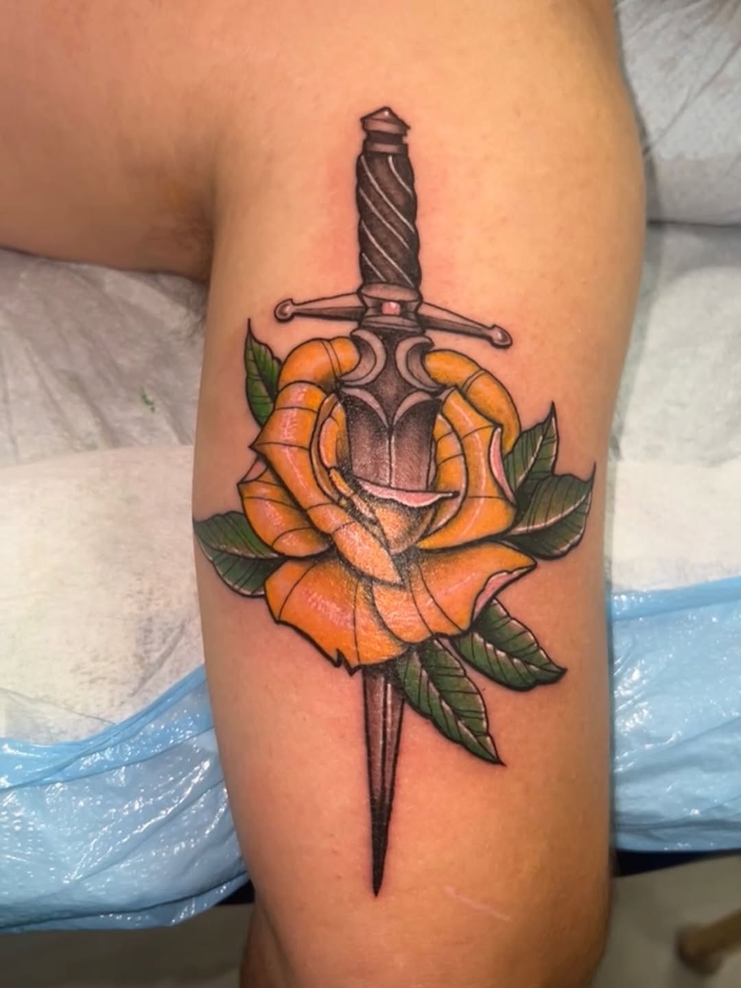 Bold dagger piercing a vibrant orange rose with leaves