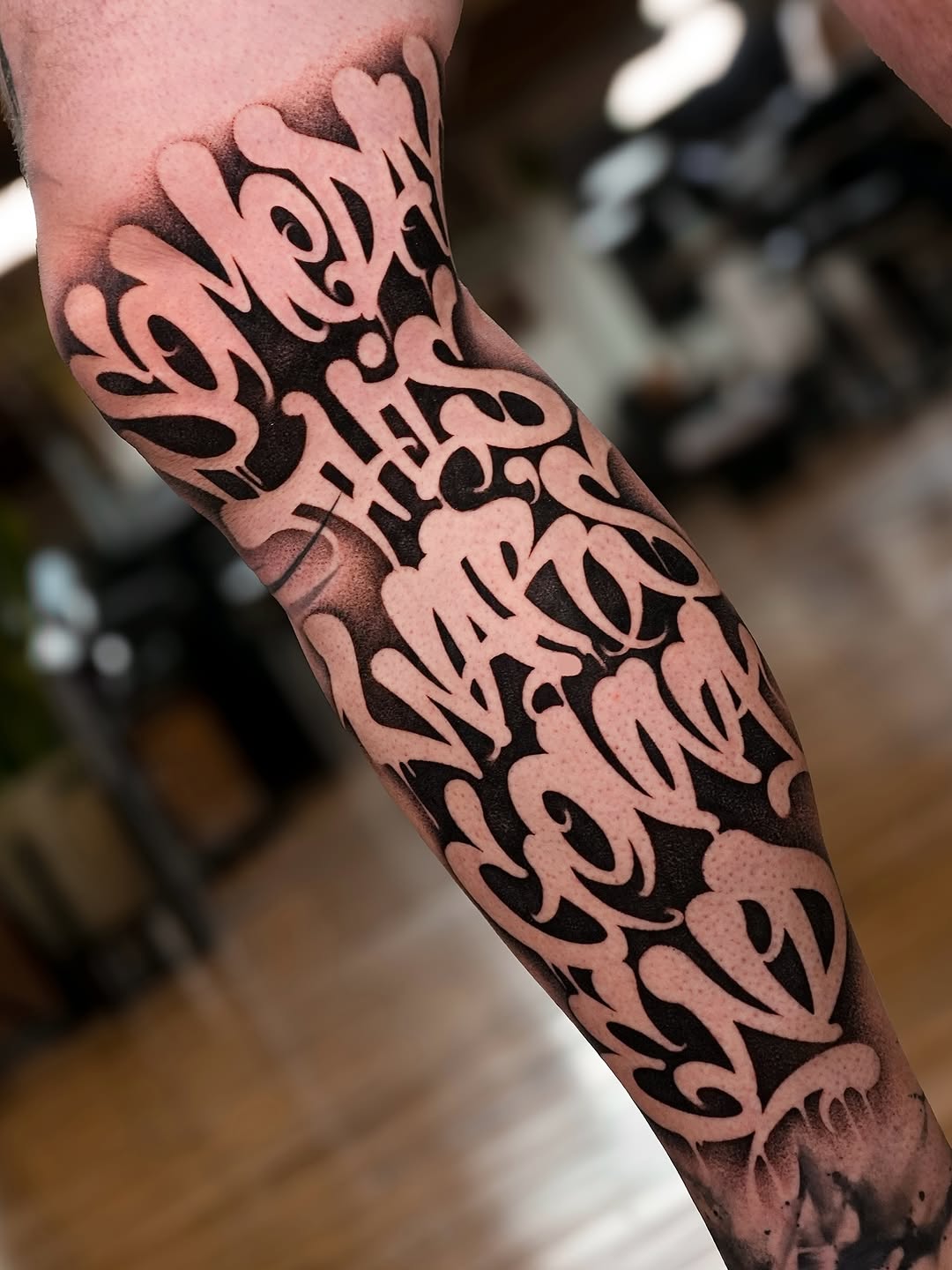 Bold negative-space graffiti lettering wraps the forearm in black.