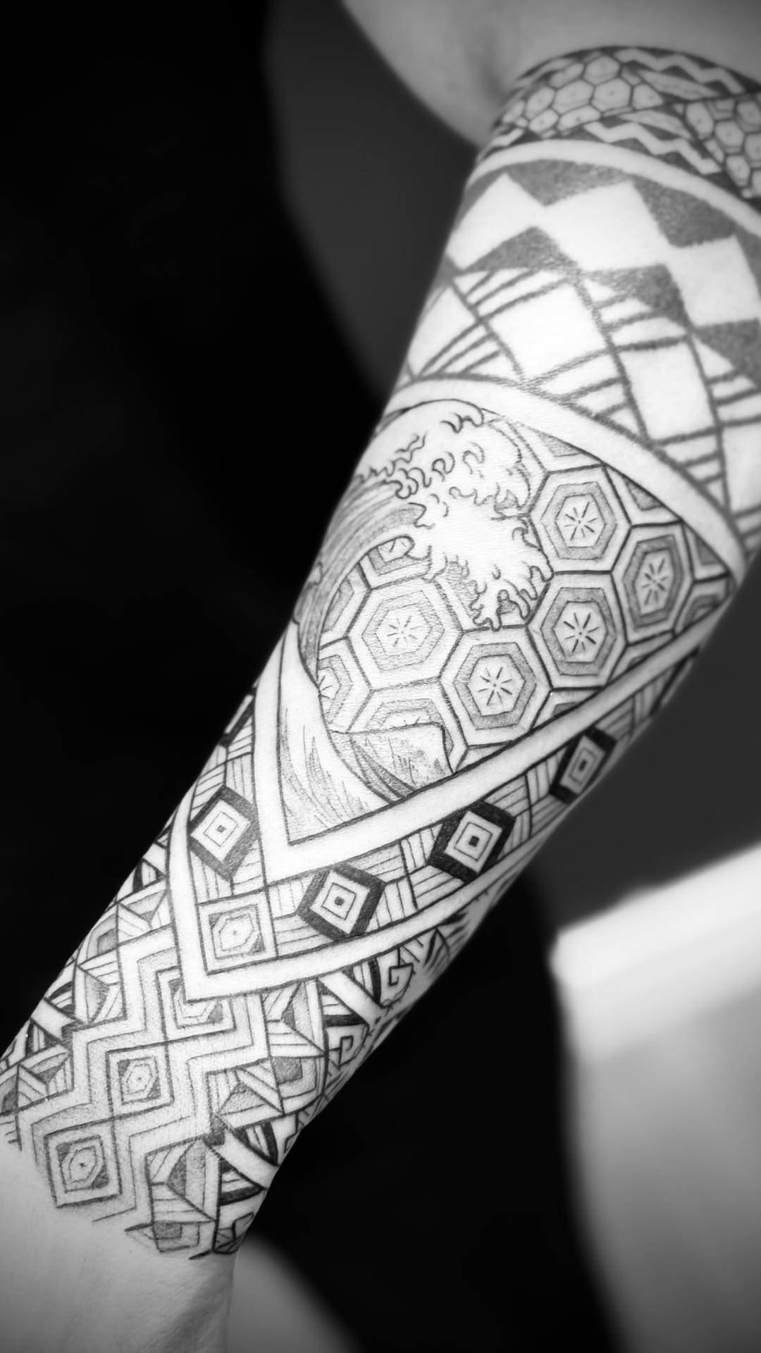 Intricate geometric forearm tattoo with hexagonal motifs and wave detail