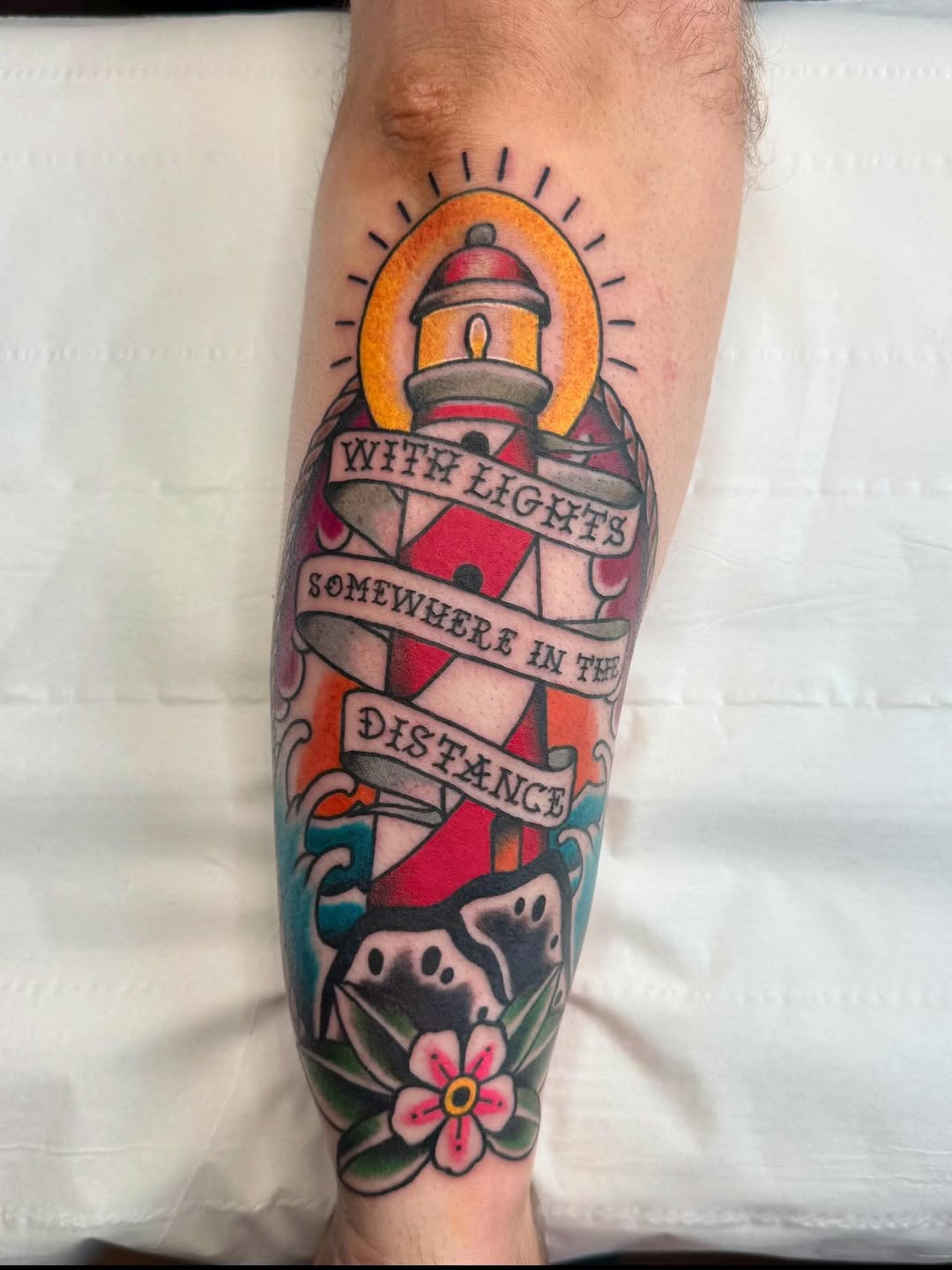 Bold traditional lighthouse tattoo with sun halo and ribbon