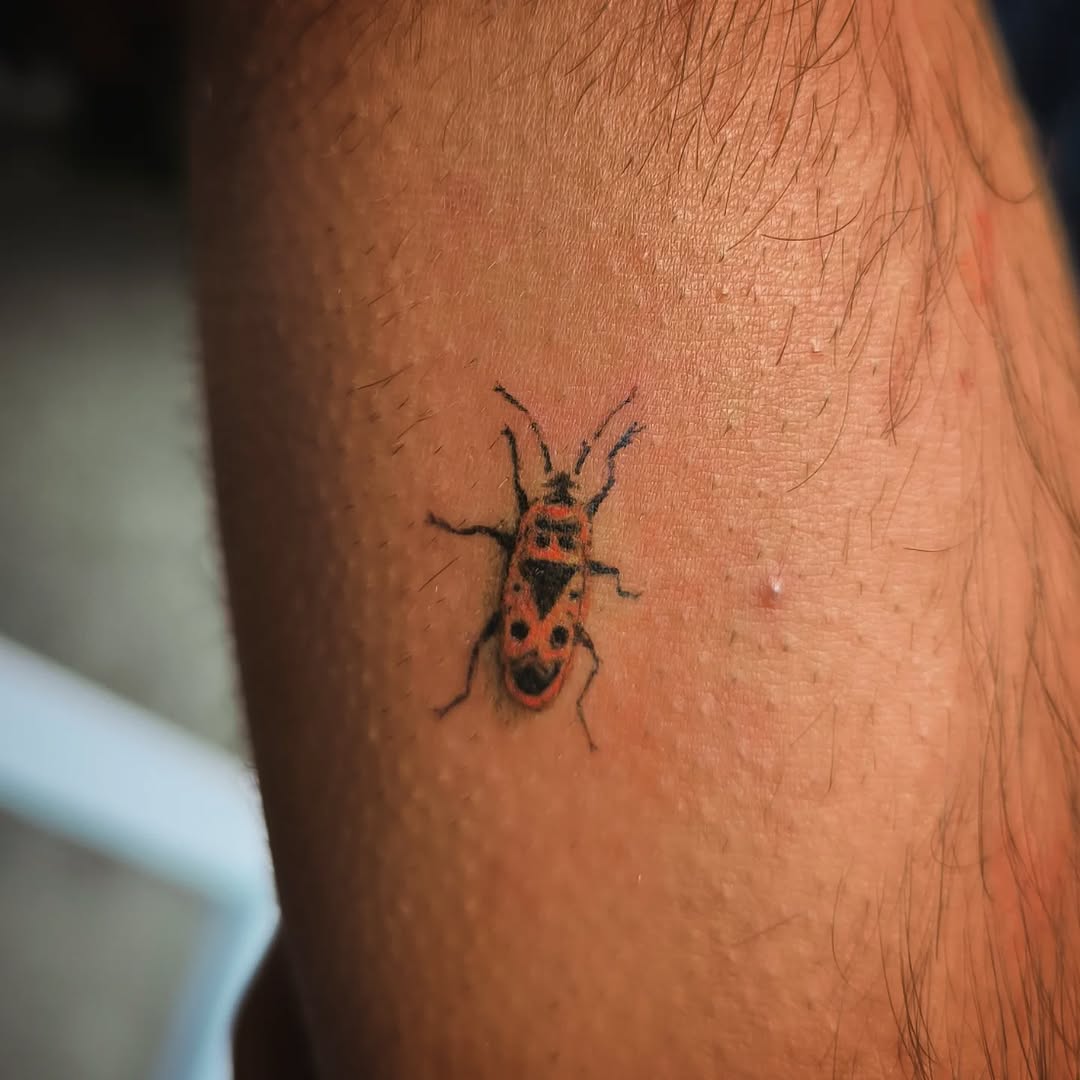 Mini red-and-black firebug beetle tattoo with fine lines