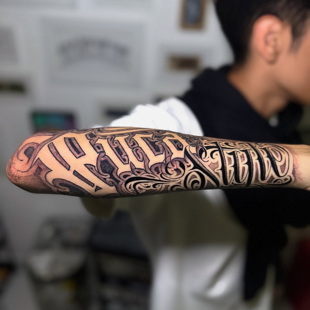 Intricate blackletter script forearm tattoo with ornate flourishes