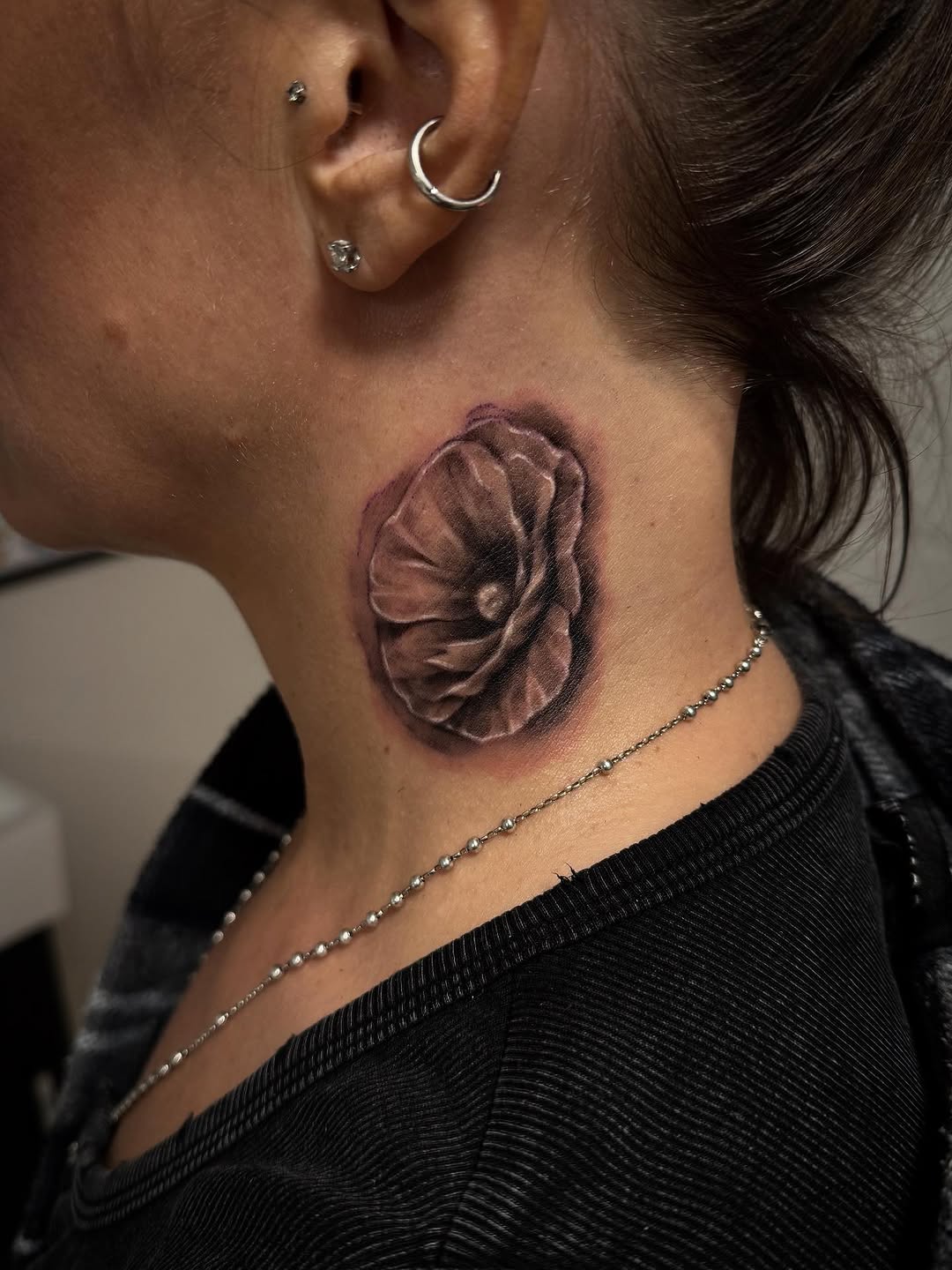Dark grayscale rose tattoo on neck with rich shading.