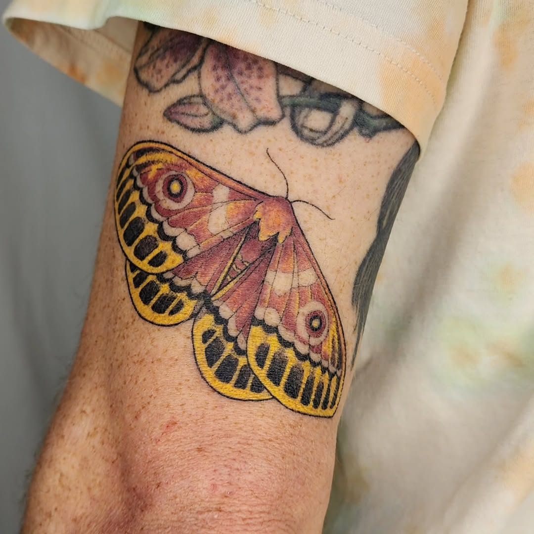 Vibrant sheep moth tattoo with pink, yellow, black wings