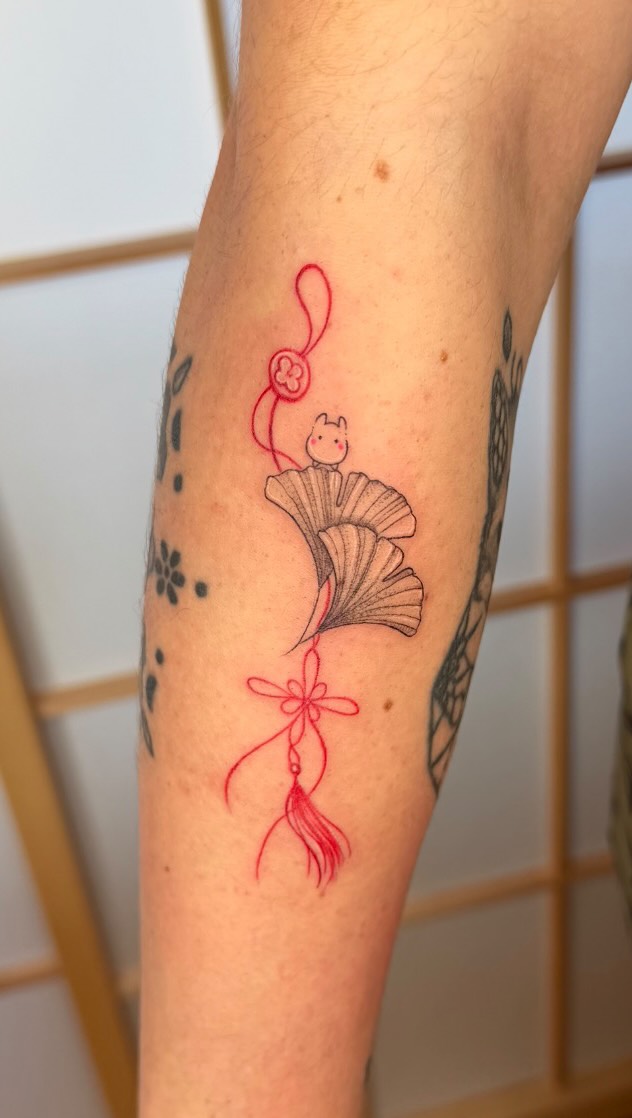 Delicate red-line Maneki-neko cat perched on ginkgo leaf